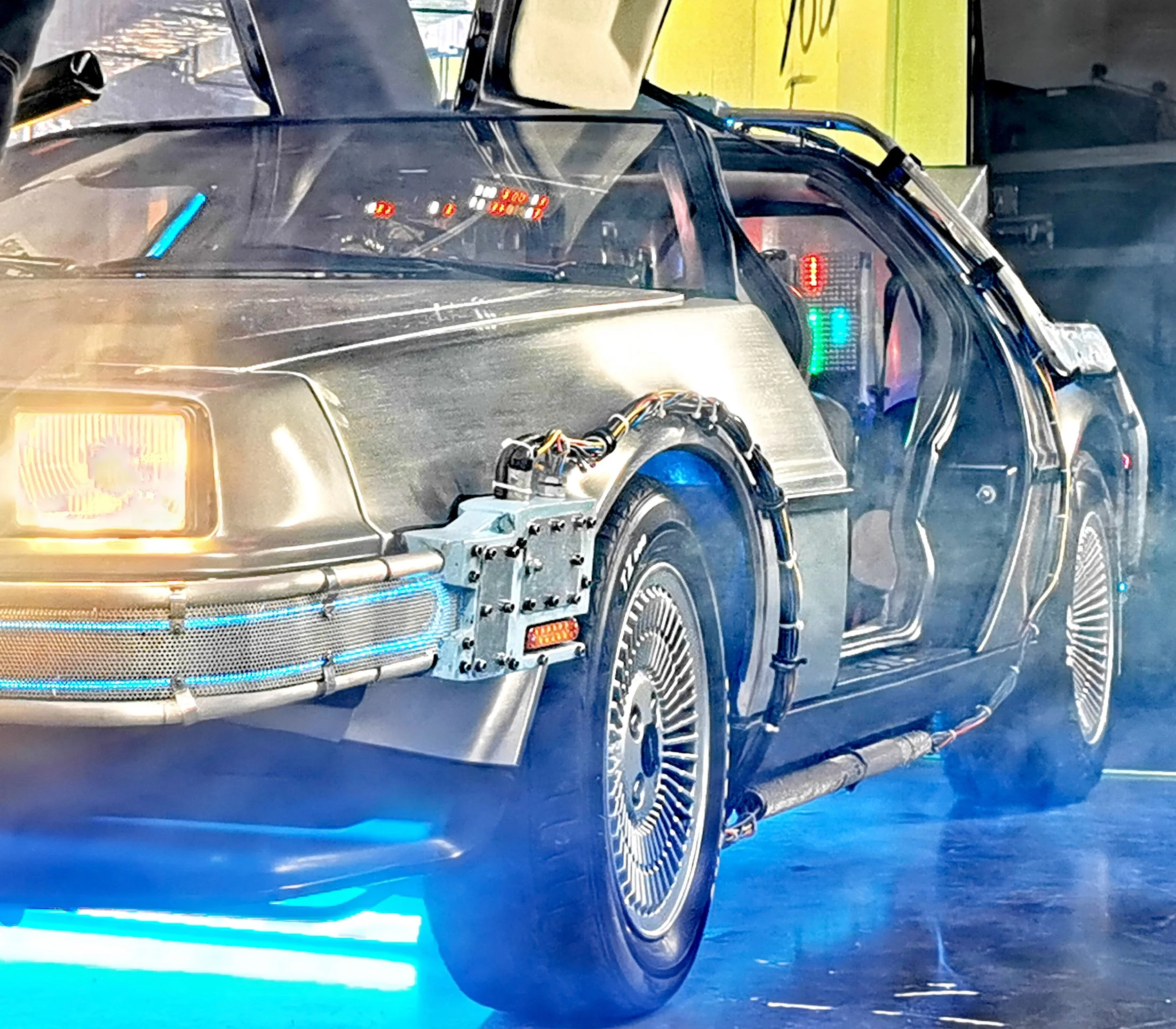 Close-up of a futuristic or sci-fi style vehicle with a sleek black exterior, illuminated blue and green LED lights, and visible electronic or robotic components on the dashboard and wheel area.