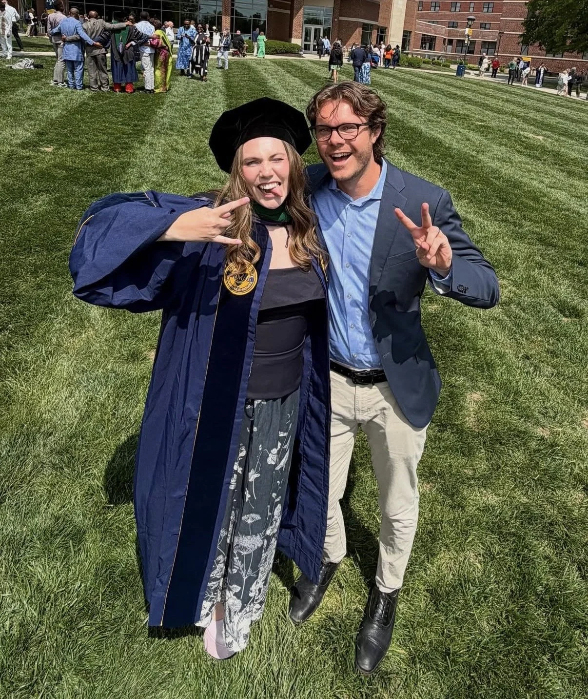Woman in graduation cap and gown with a man, making faces at the camera