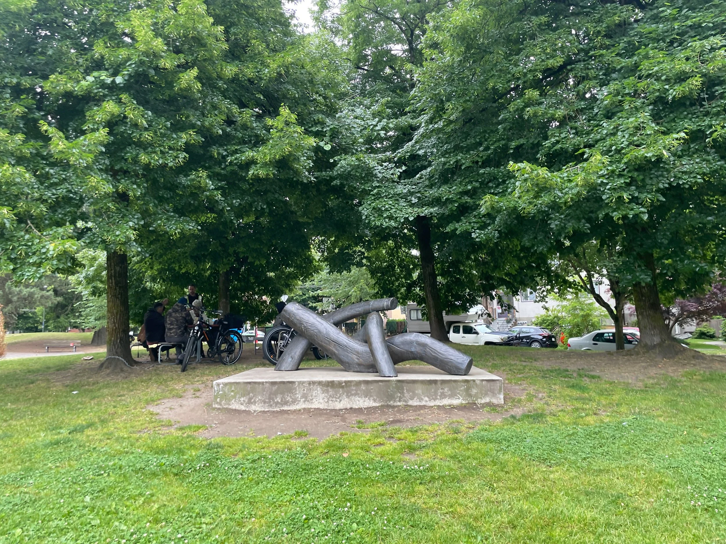  the original  Dude Chilling : the sculpture Reclining Figure by Michael Duncan, under trees in Guelph Park. It is a slightly larger than human size abstract figure, reclining in a sassy pose, one leg flung over the other. It looks like it is made of