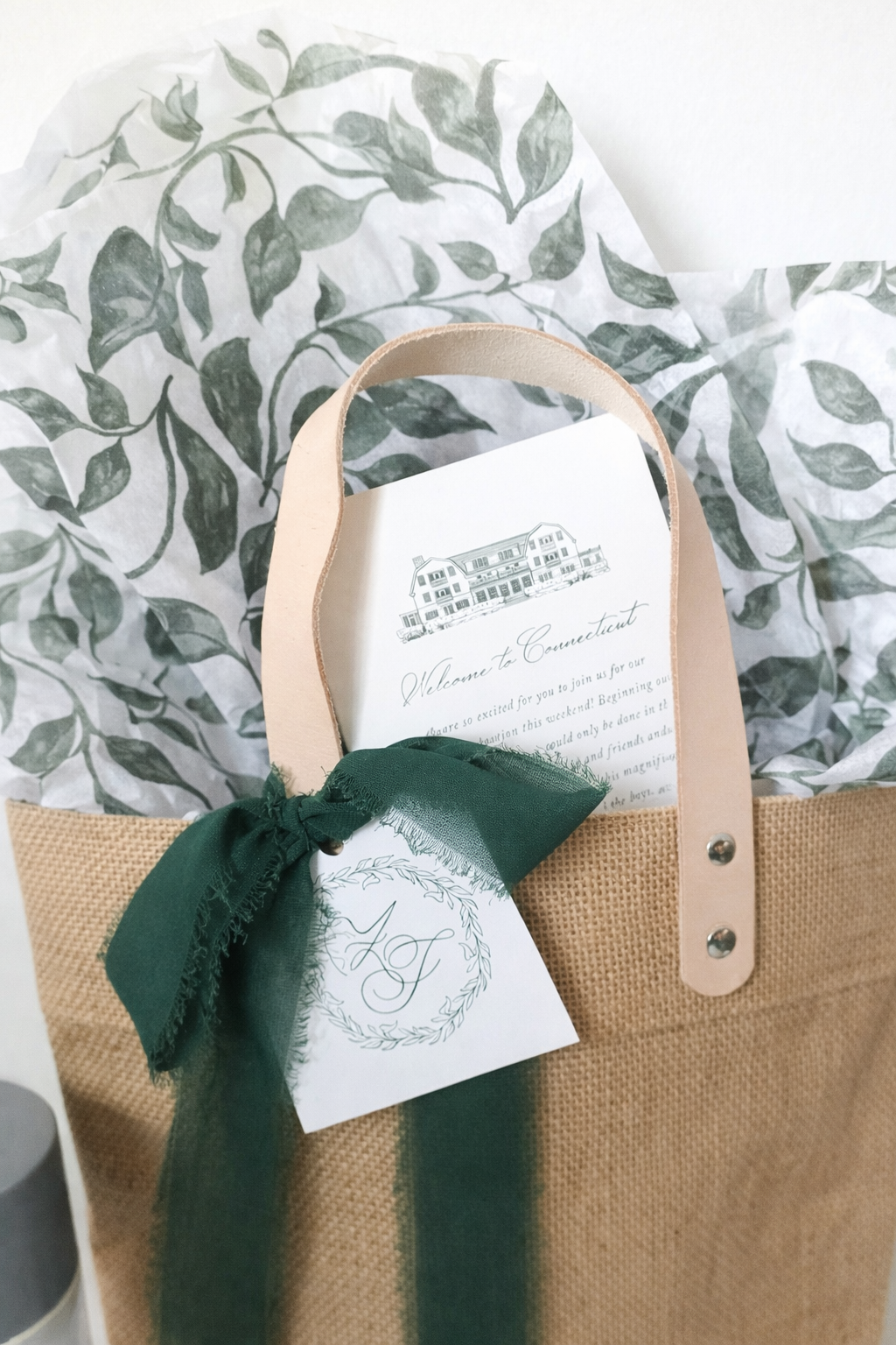 Fully packaged custom wedding welcome bag for an Auberge Mayflower Inn wedding in Washington, CT with jute tote, hunter green ribbon, custom monogram tag and printed welcome note.