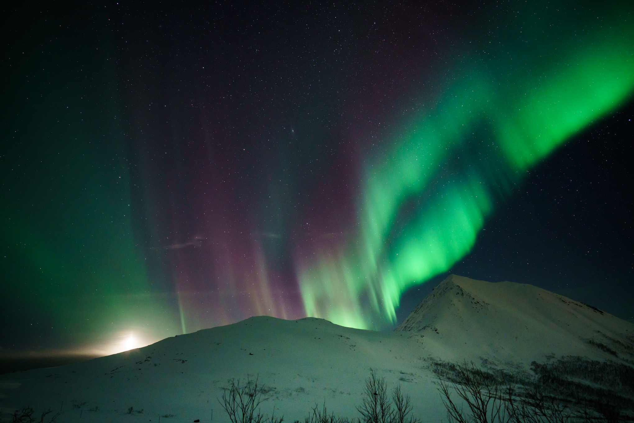 On my last night in Norway, the moon peaked out over the mountain we were on accompanied by the Aurora Borealis to say goodbye. Sharp peaks in auroral activity often bring out the red/purple colors along with the more common green streaks.