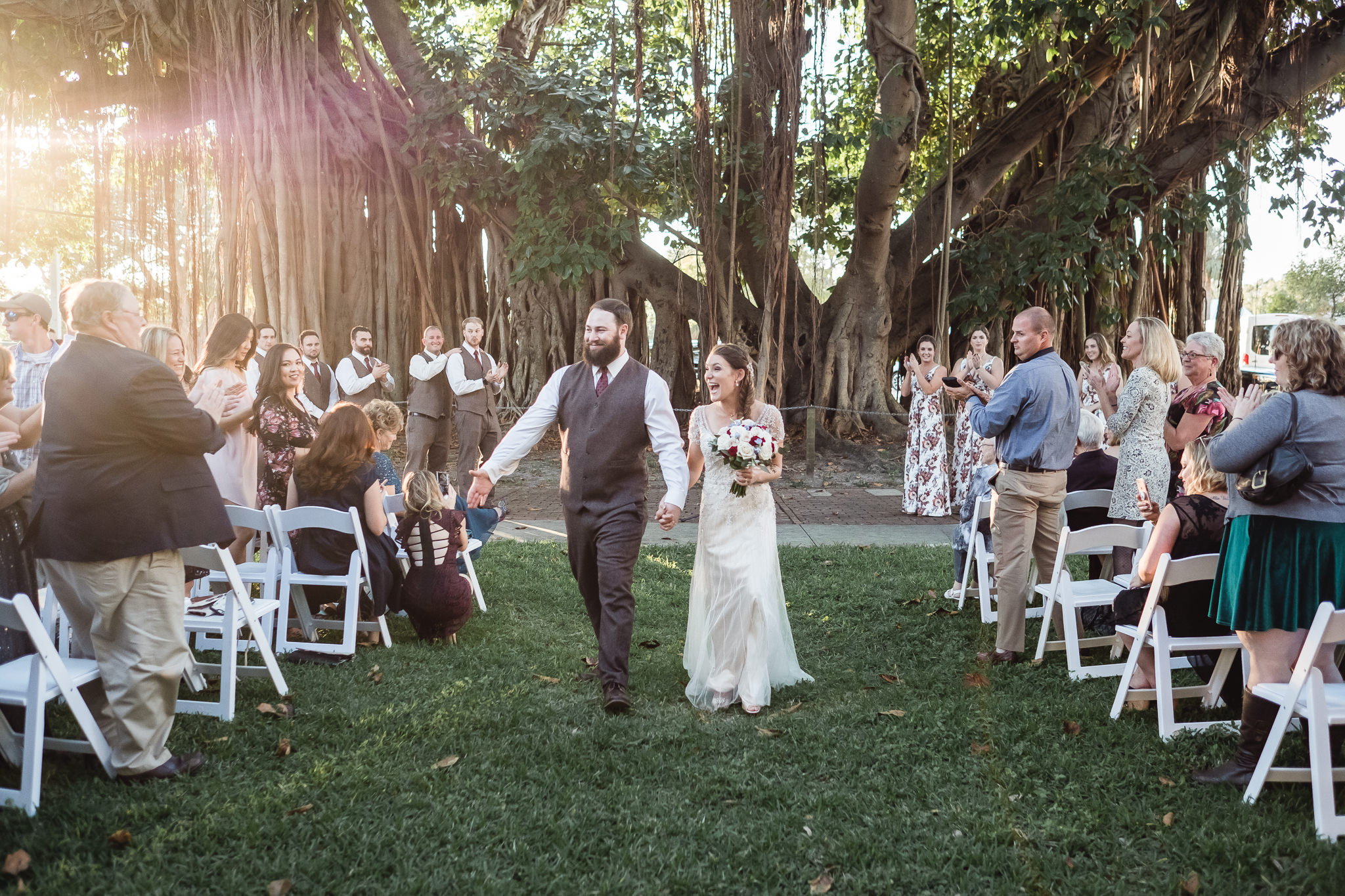 wedding photograph of a joyous bride and groom leaving their ceremony by a Banyan tree near Mirror Lake Park in St. Petersburg, Florida