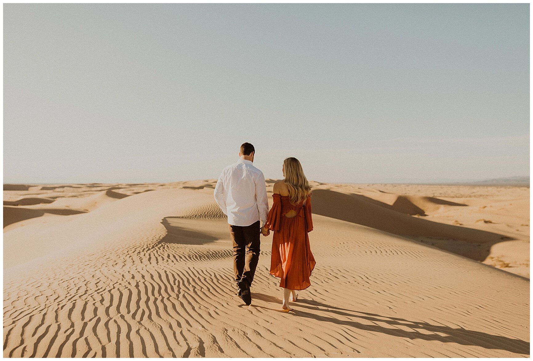  engaged couple walking along sand dunes 