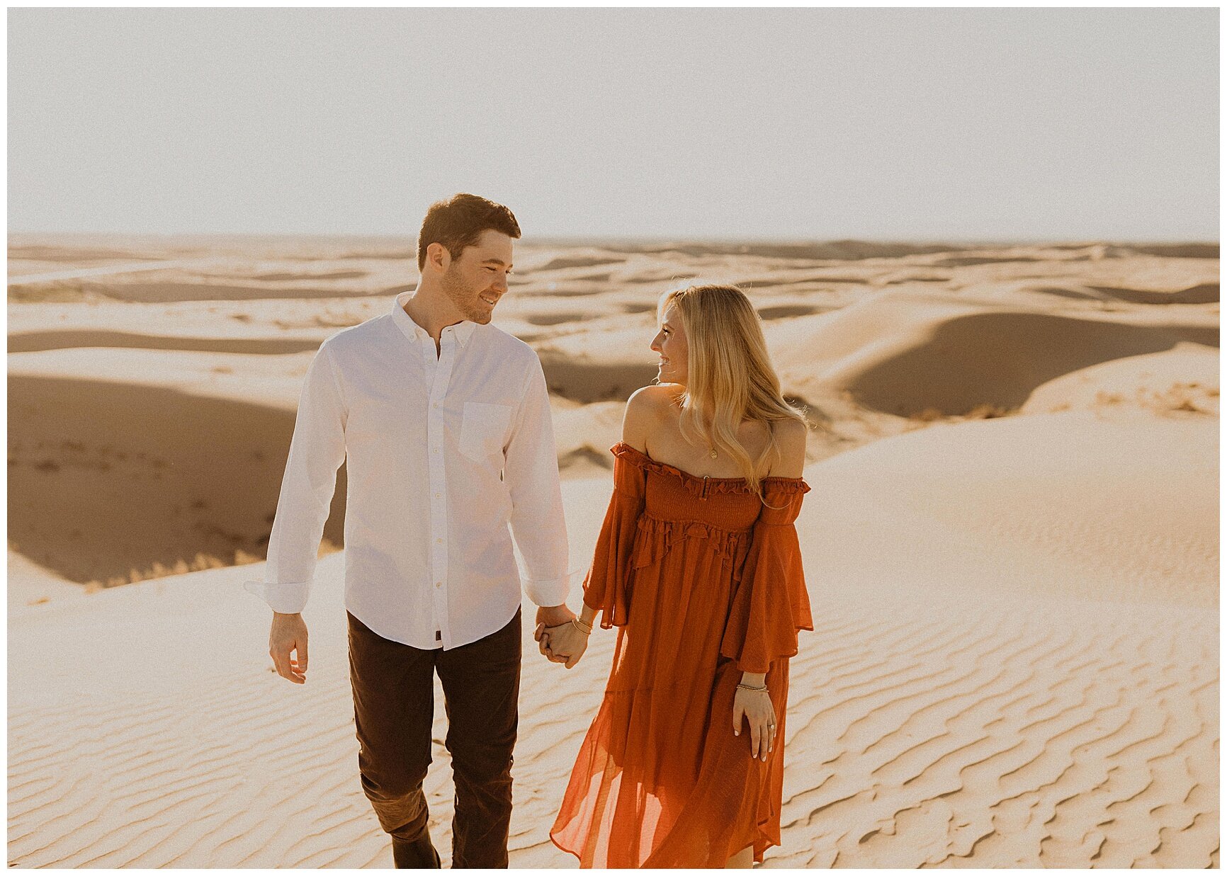  engaged couple walking along sand dunes 