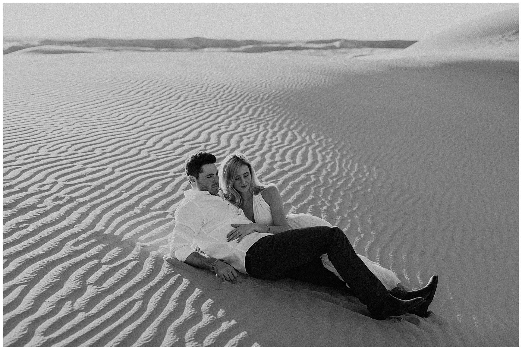  engaged couple laying in the sand during their sand dune engagement session 