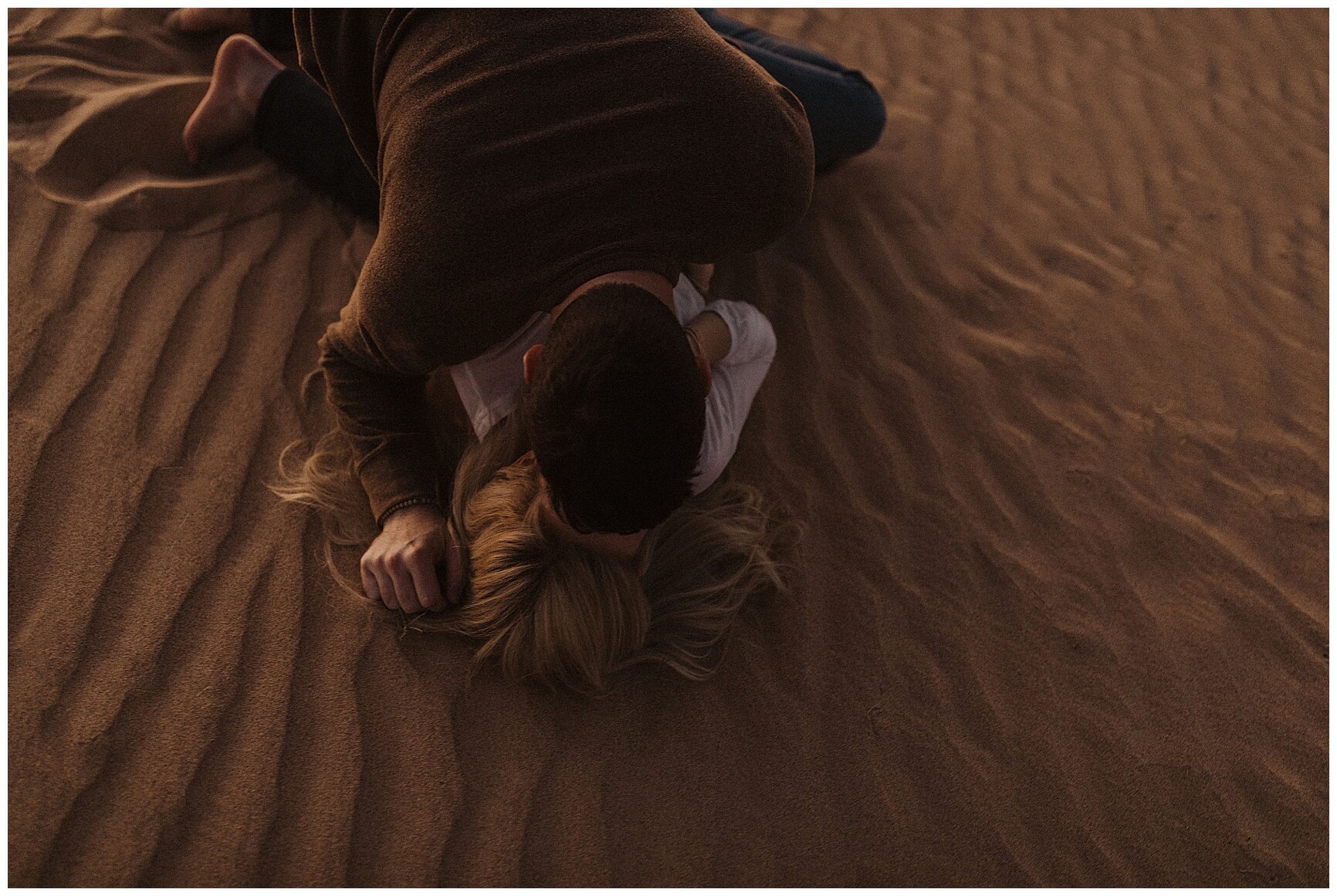  engaged couple laying in the sand during their sand dune engagement session 
