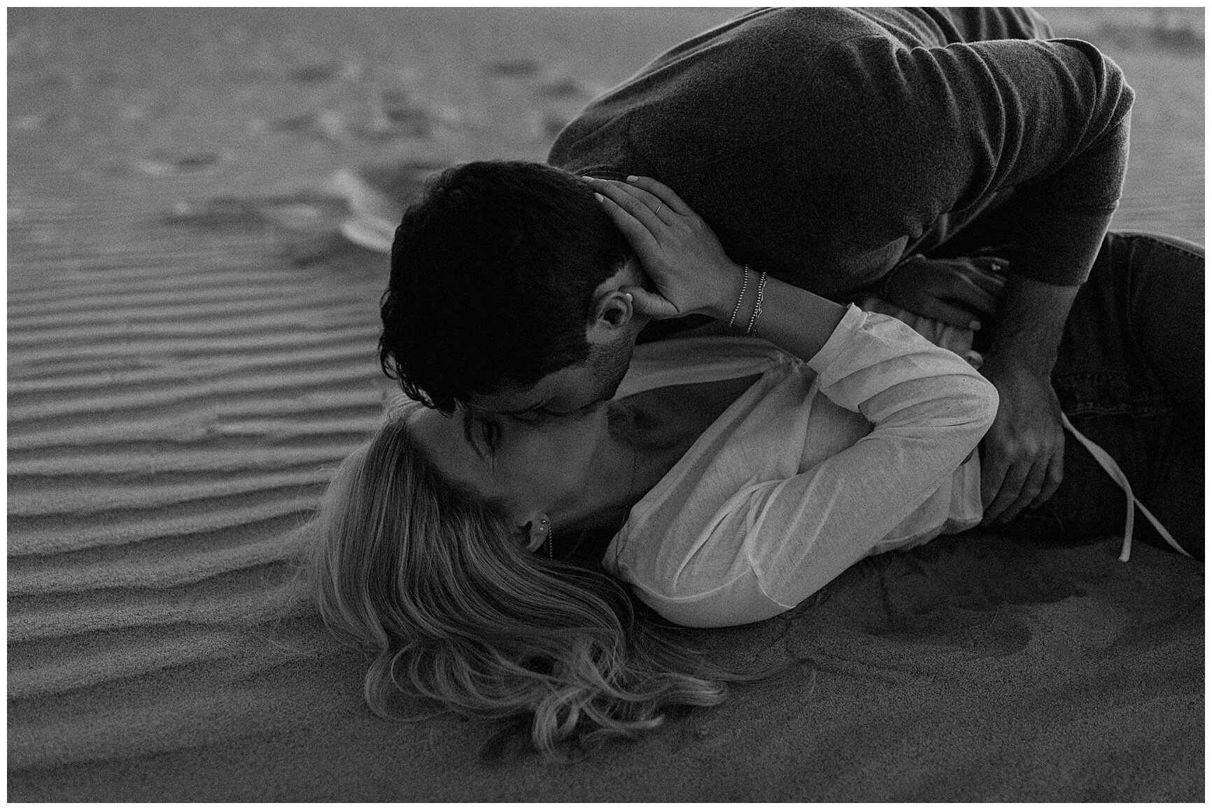  engaged couple popping champagne in the sand during their sand dune engagement session 