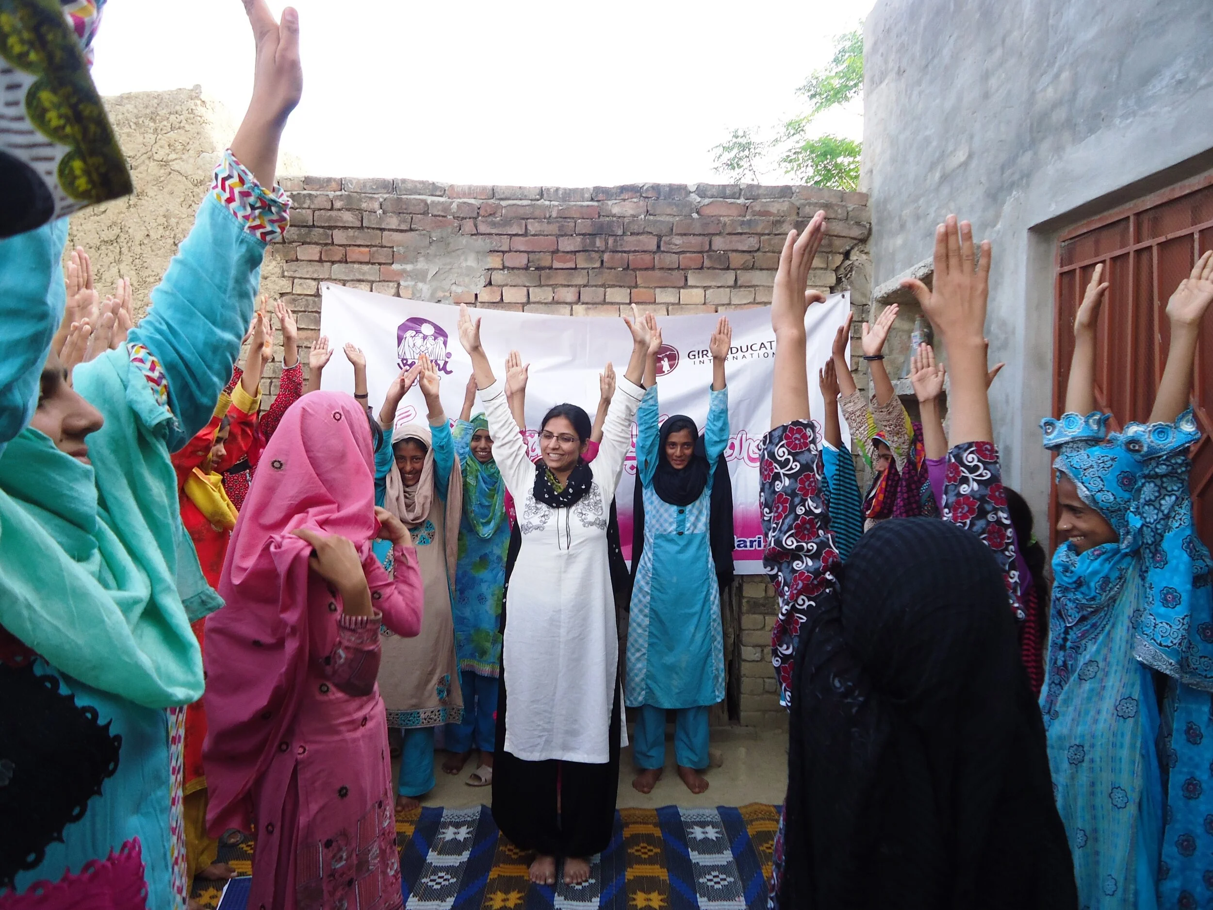 A group of girls in Pakistan holding their hands up in the air in celebration and smiling after a self-growth workshop