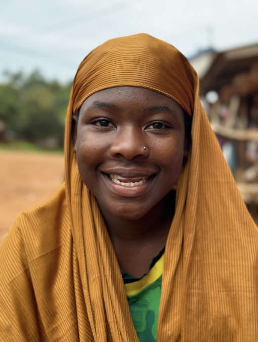 Smiling female student in Tanzania, wearing a green tshirt and gold head scarf