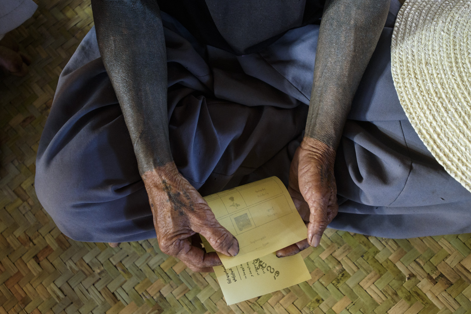 A villager with traditional Buddhist tattoos practices voting with a mock ballot. Many in the town, accessible only by a muddy mountain pass, will be voting for the first time.