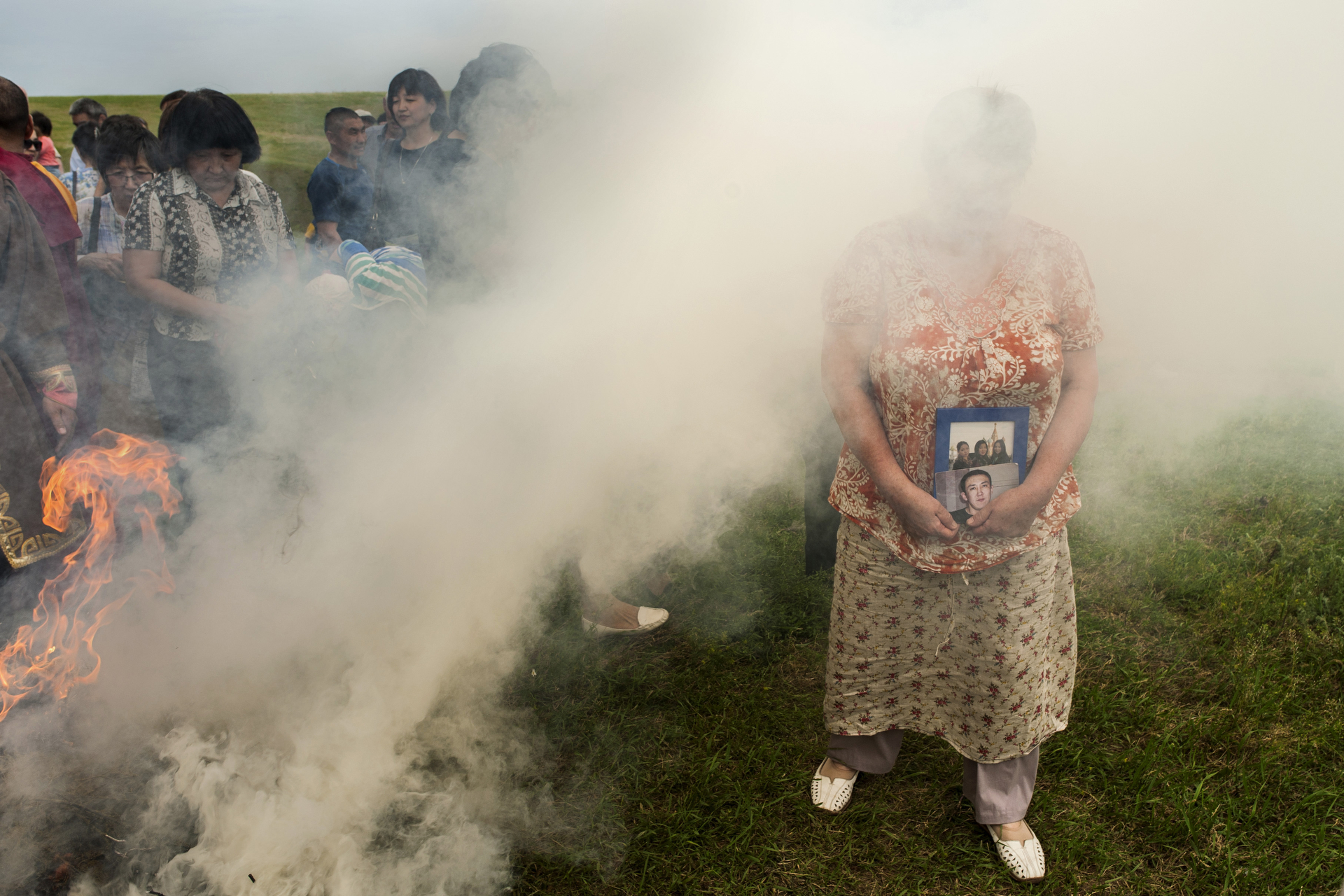  A woman carrying pictures of her beloved ones is walking trough a sacred bonfire smoke. It's believed this buddhist ritual gives good luck and fortune. Elista, Russia, May 2016. 
