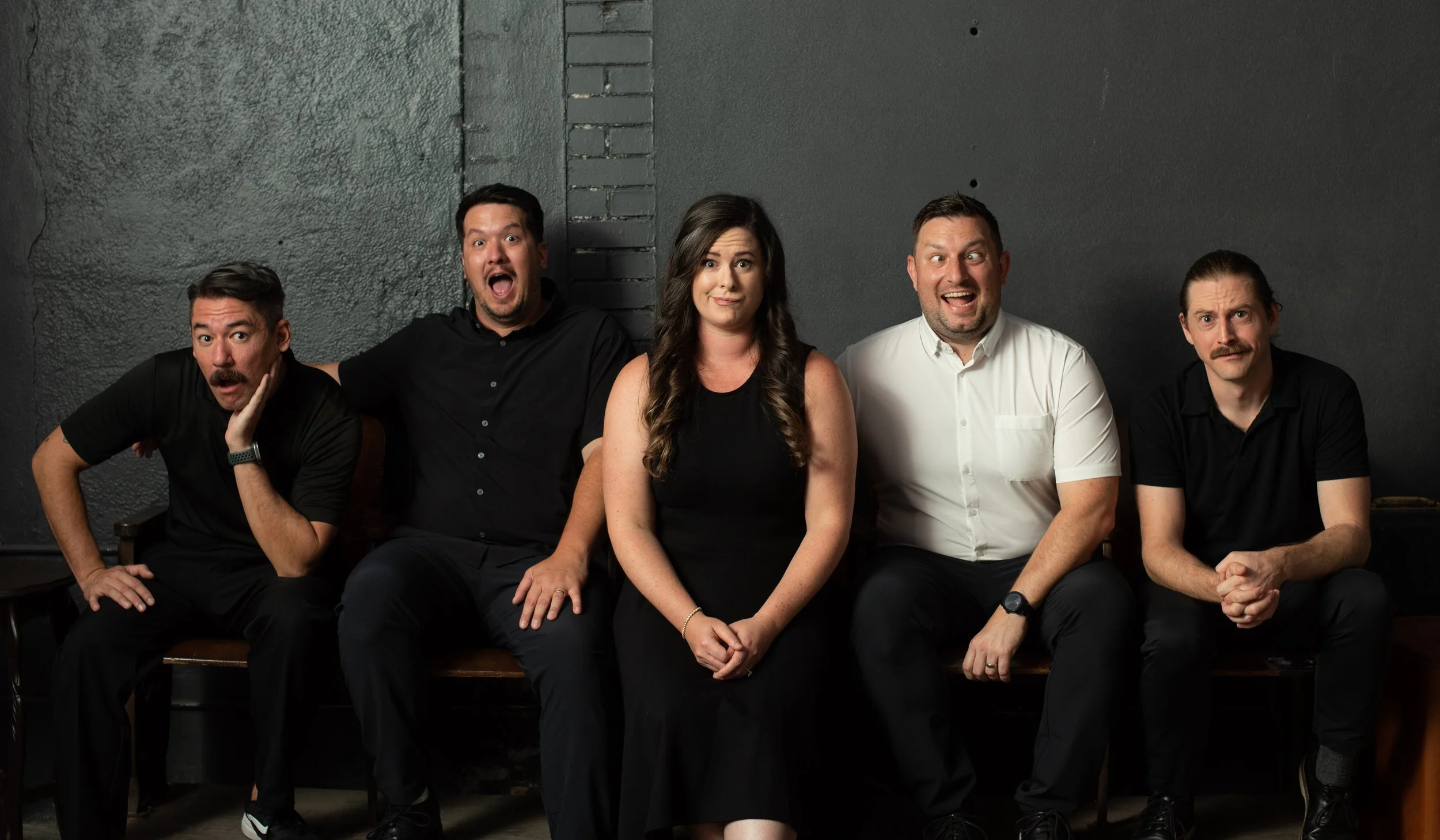 The Imagery Wedding Films filmmaker Team. A group of five people sitting on a bench against dark wall, making expressive faces and gestures.