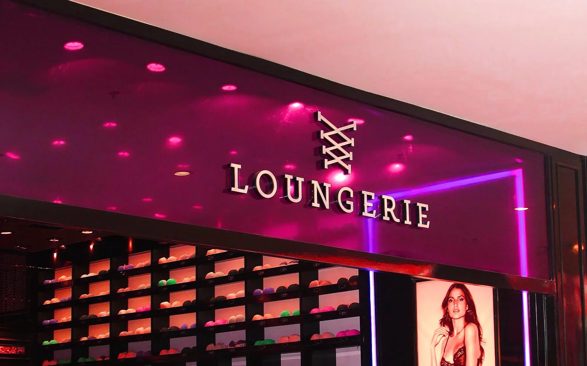Letreiro dourado da Loungerie em fachada iluminada com neon rosa e roxo.webp