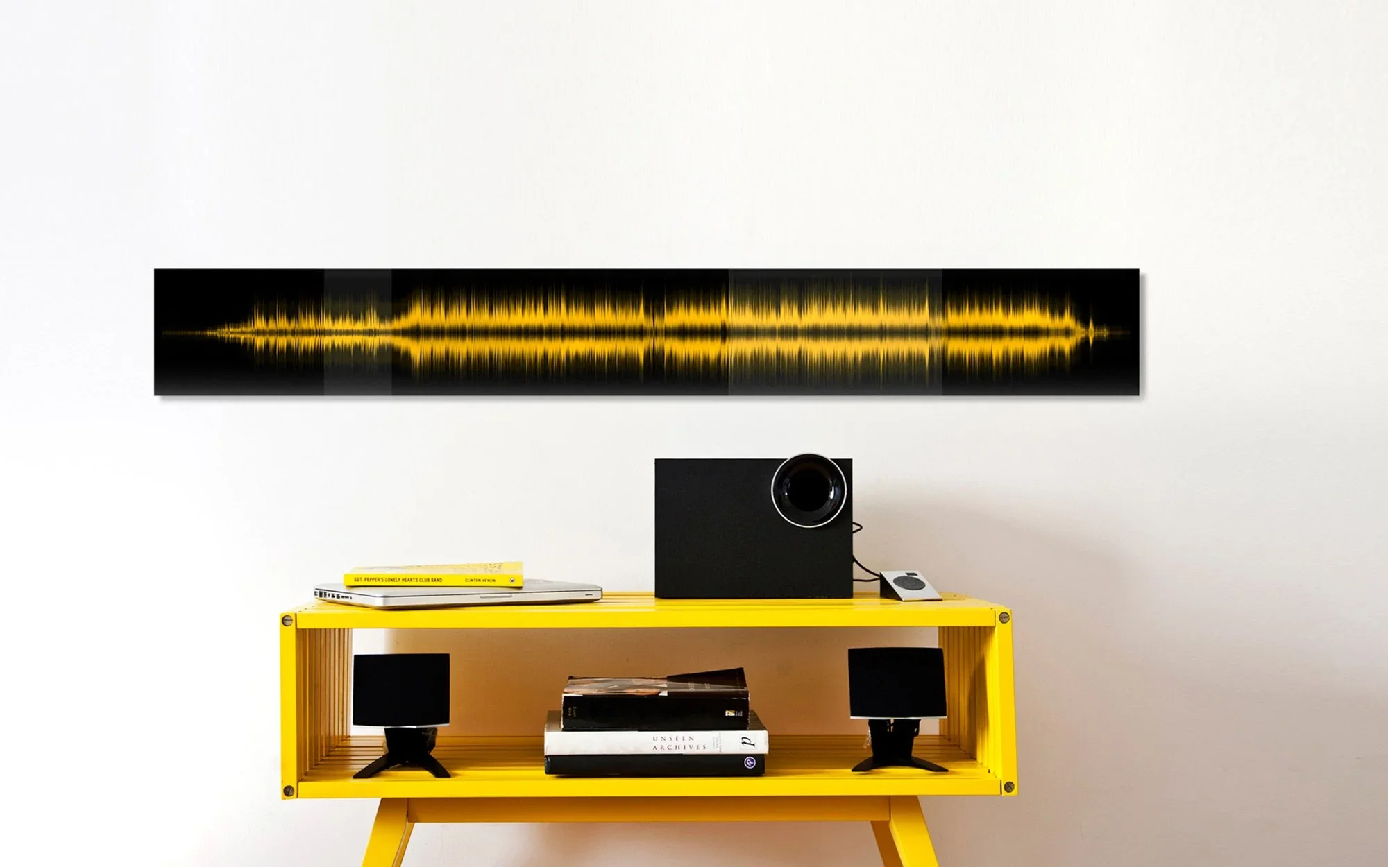 Quadro com visualização de onda sonora amarela na parede, sobre mesa amarela com caixa de som preta e vinil dos Beatles.webp