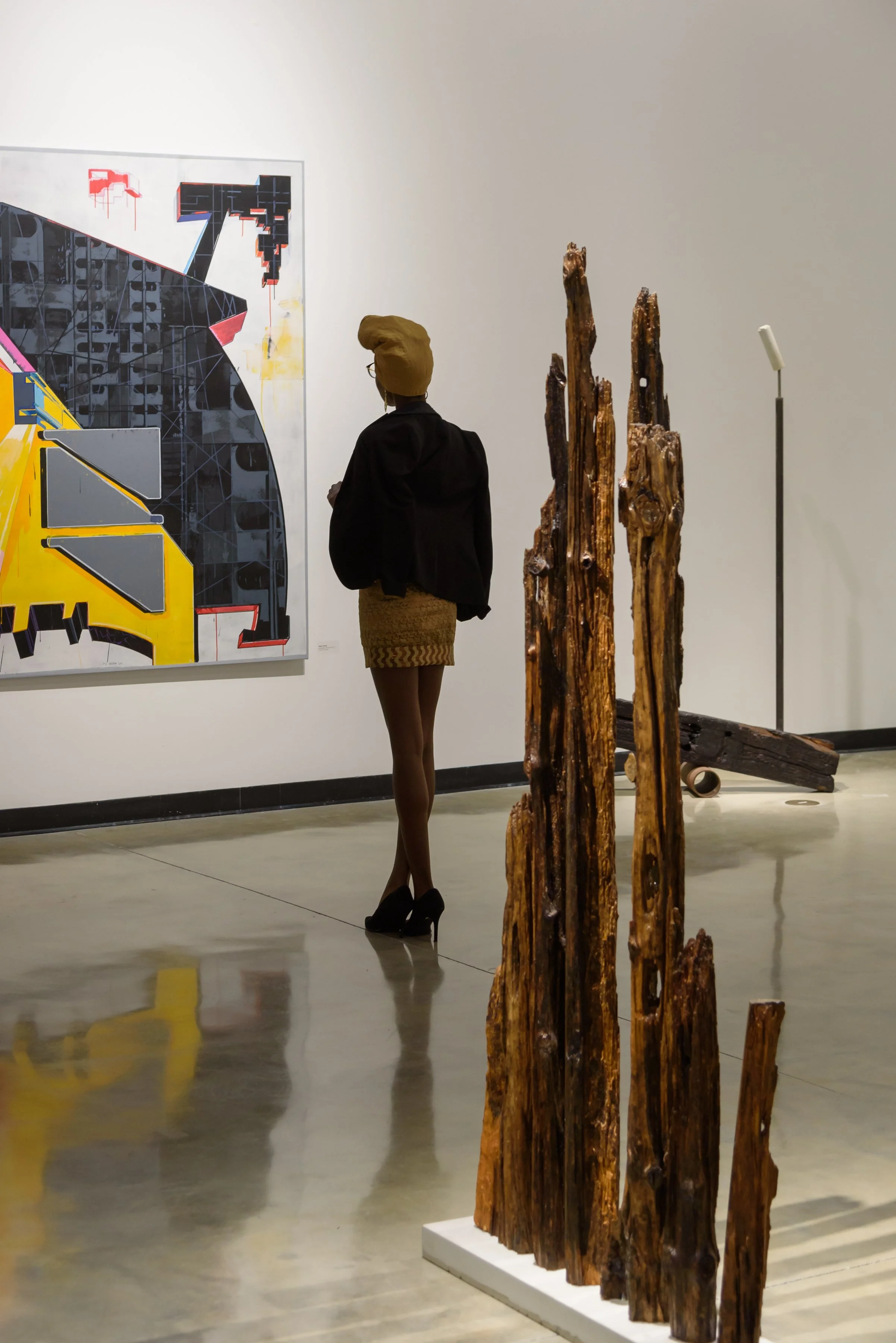 Sculpture by Norman Silva called City Scape. It's made of 7 vertical decaying pieces of wood, placed vertically on a long, rectangular concret base.