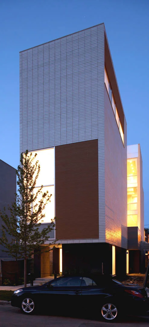 Single-Family Location: Chicago, IL Photos: Marty Peters Program This custom residence was created out of the basic elements in architecture-light, shadow, massing, color, transition and how we experience these things. The owner requested one thing; “…create a home that no matter my mood or frame of mind, it makes me forget even my worst day in calming surroundings filled with light”. The intention was to create a light filled retreat in a tight urban setting. A residential Light Box. The residence is located on a narrow urban lot in Chicago's older Bucktown neighborhood. It is for a young urban couple. The residence faces east and is bound on its north and south by neighboring buildings as close as three feet, rising four stories. The size of the house was to be approximately 6000 square feet in area and comprise of 4 levels. Because the residence was to be four stories, the main living level was located on the second floor, taking advantage of the garage roof as exterior urban space. The first level required an office for the owners, a den, an exercise room and spa bath. The second floor required a living room, dining room, kitchen and family room. The third floor was for the bedrooms and an open reading loft. The fourth floor was for the master bedroom suite, and the roof level was for entertaining, including a full roof deck with views of the city skyline. The owners also requested a series of exterior spaces located on different levels; courtyard, garage roof deck and house roof deck. Solution The design solution started with an urban box and the notion of “light” and how to move light throughout the house. The box was given carved openings on the ends in addition to a large hidden inner light court that introduces natural sunlight into the center of the residence. Because the entire residence is conceived of as one solid rectangle, openings in it and carved areas shift its scale, drawing attention to its subtle detail. Windows for different rooms were grouped to strengthen the shift in scale. The first floor was also set back, carved and clad in dark masonry to give hierarchy to its upper white masonry clad main levels. The masonry is carefully articulated in a stacked bond pattern reinforcing the orthogonal nature of the residence. This residence is designed using very simple strategies. The exterior is mainly clad in only two materials; white masonry and cedar, with a small amount charcoal masonry used at the first floor base. The white masonry creates open and light filled interiors while the cedar is used as natural, softening accent. Both materials extend to the interiors to create subtle contrasting surfaces and blur the boundary between the exterior and the interior.