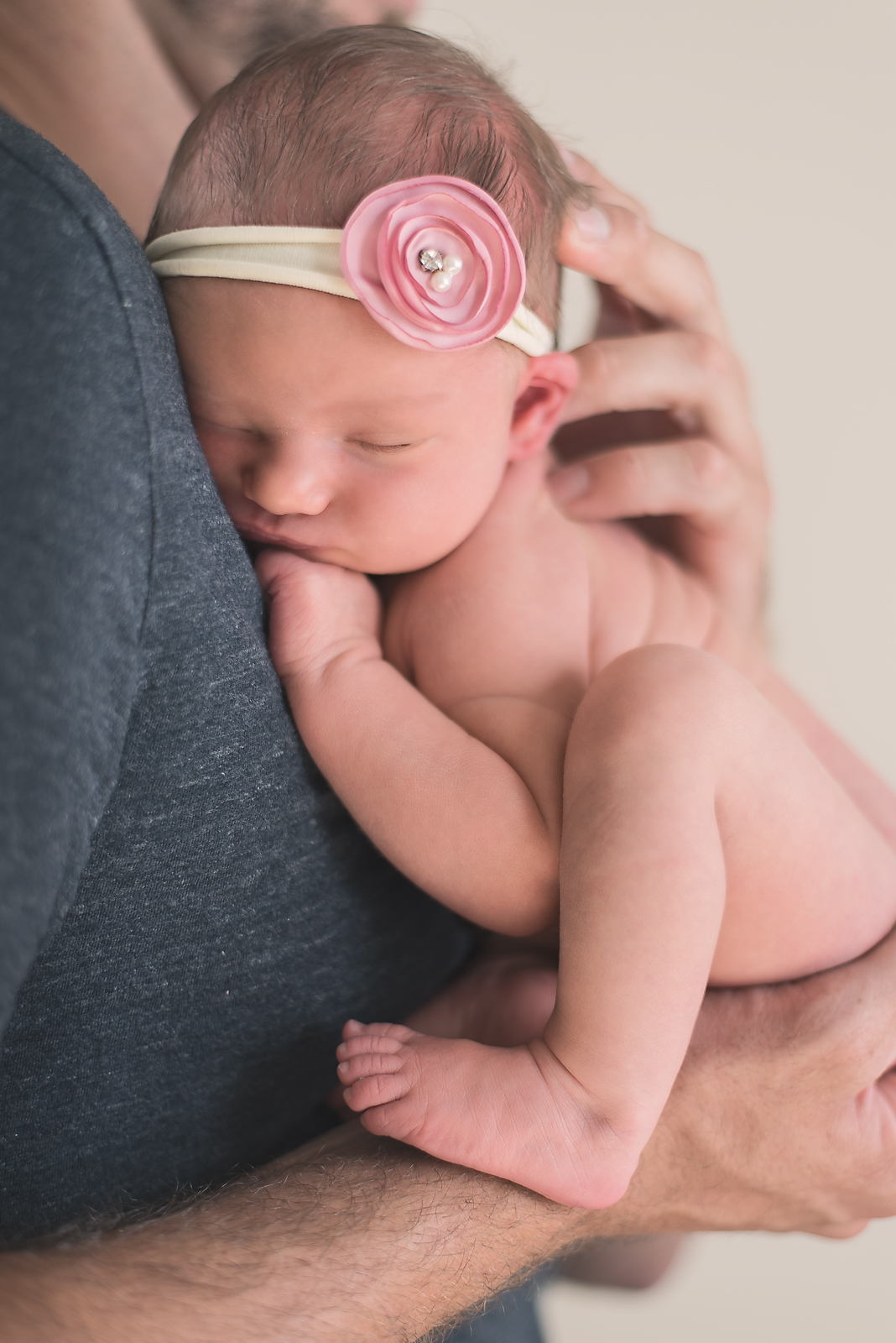 naked newborn in daddys hands with headband