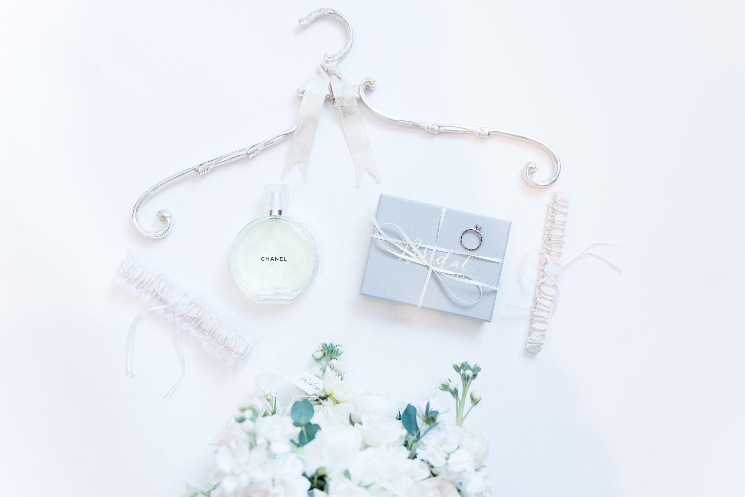 wedding day detail photograph with perfume, rings, hanger, garter, and flowers