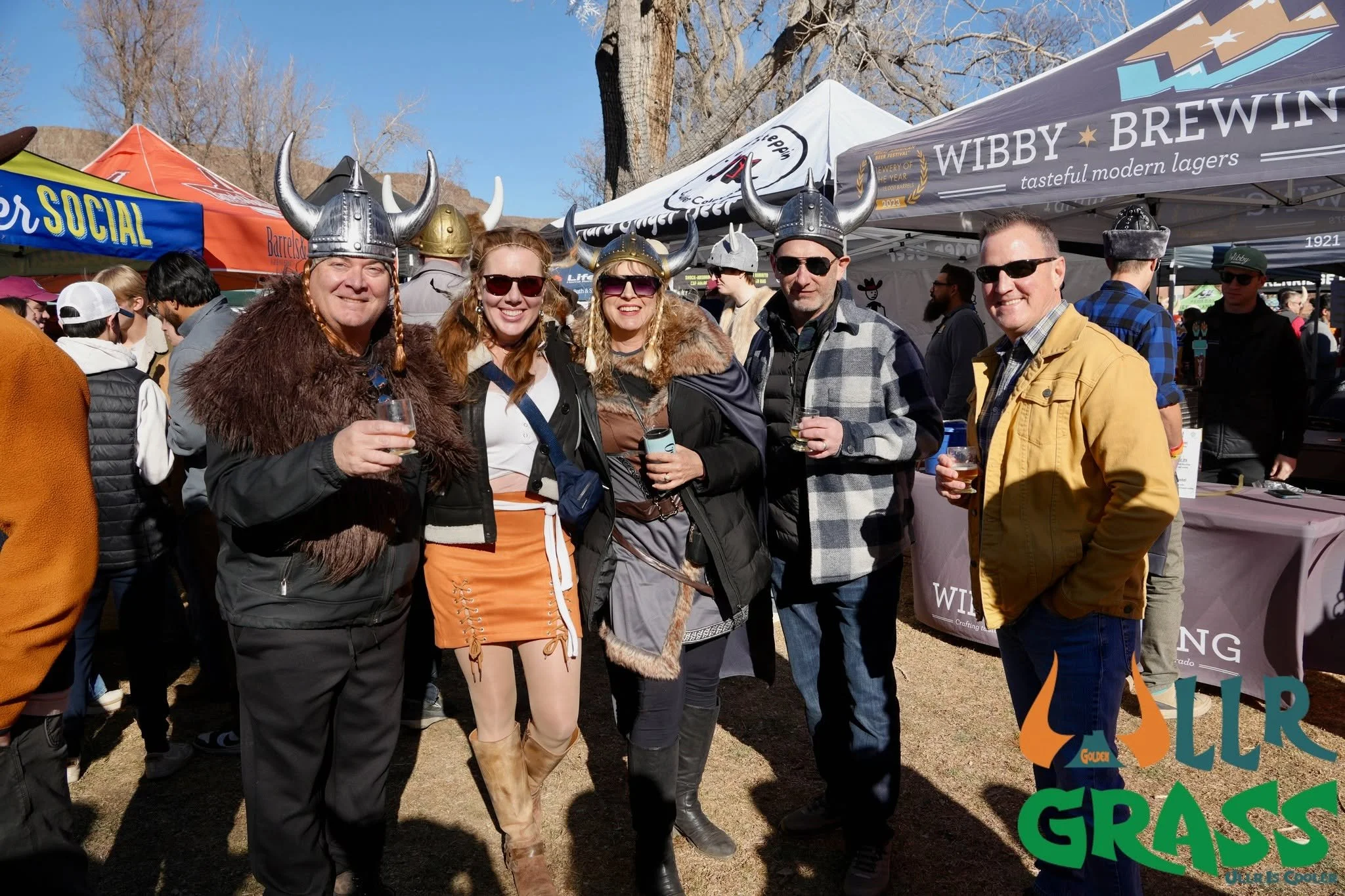 Group of people dressed in Viking costumes attending an outdoor event on a sunny day, with tents and trees in the background.
