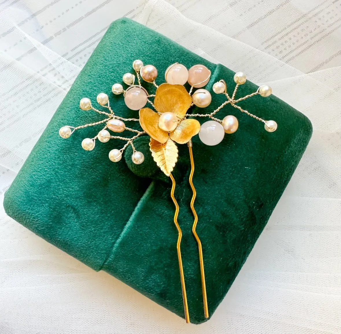A beautiful bridal hairpin made with pearls and a brass flower on a green velvet box.
