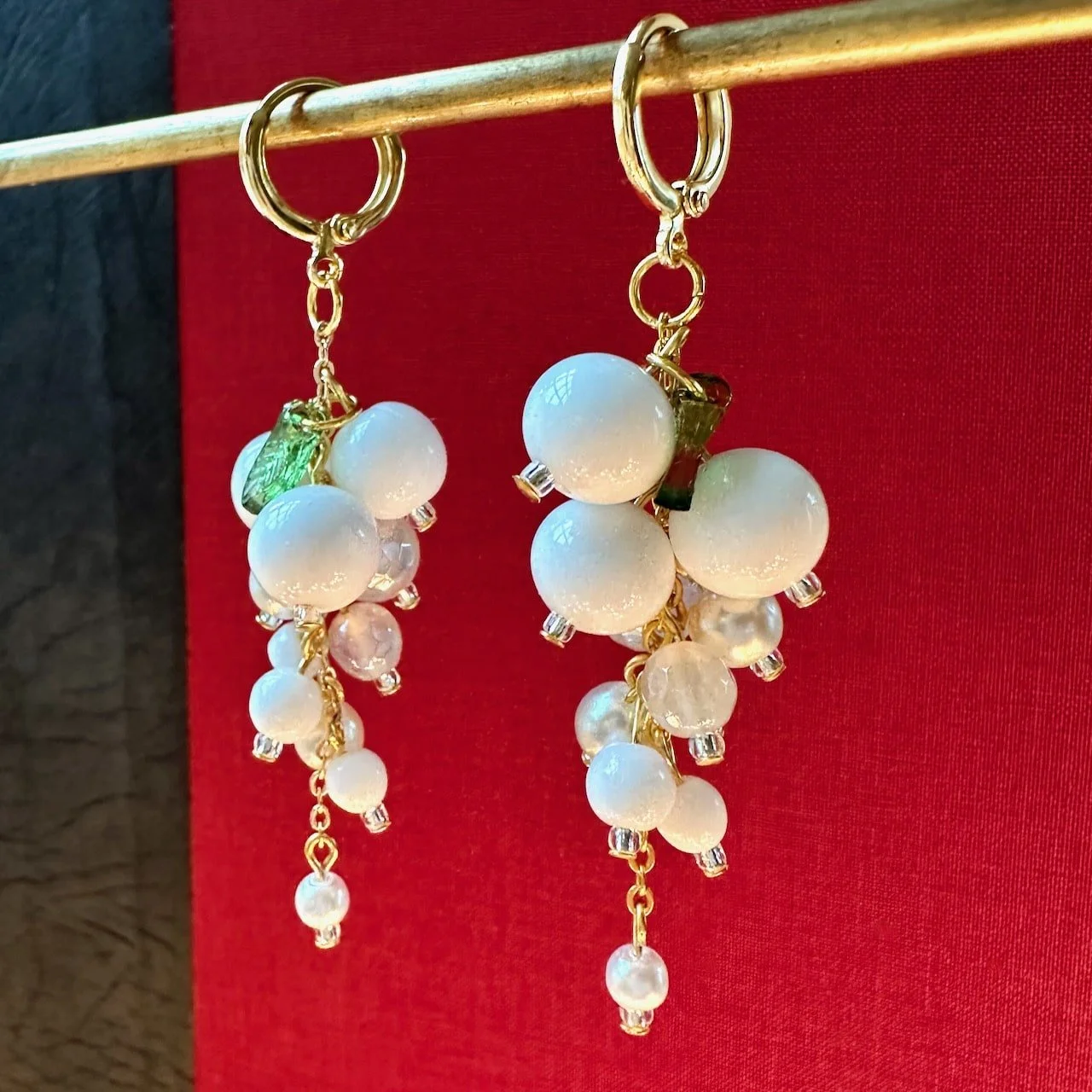 white bead dangle earrings on a red background, with green leaf.