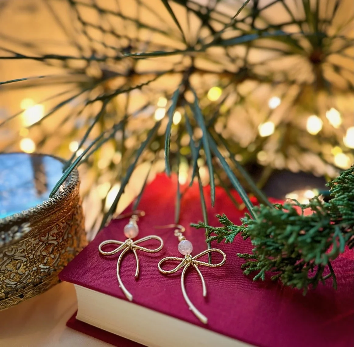 Golden bow earrings with mystic agate on a red book with Christmas lights.