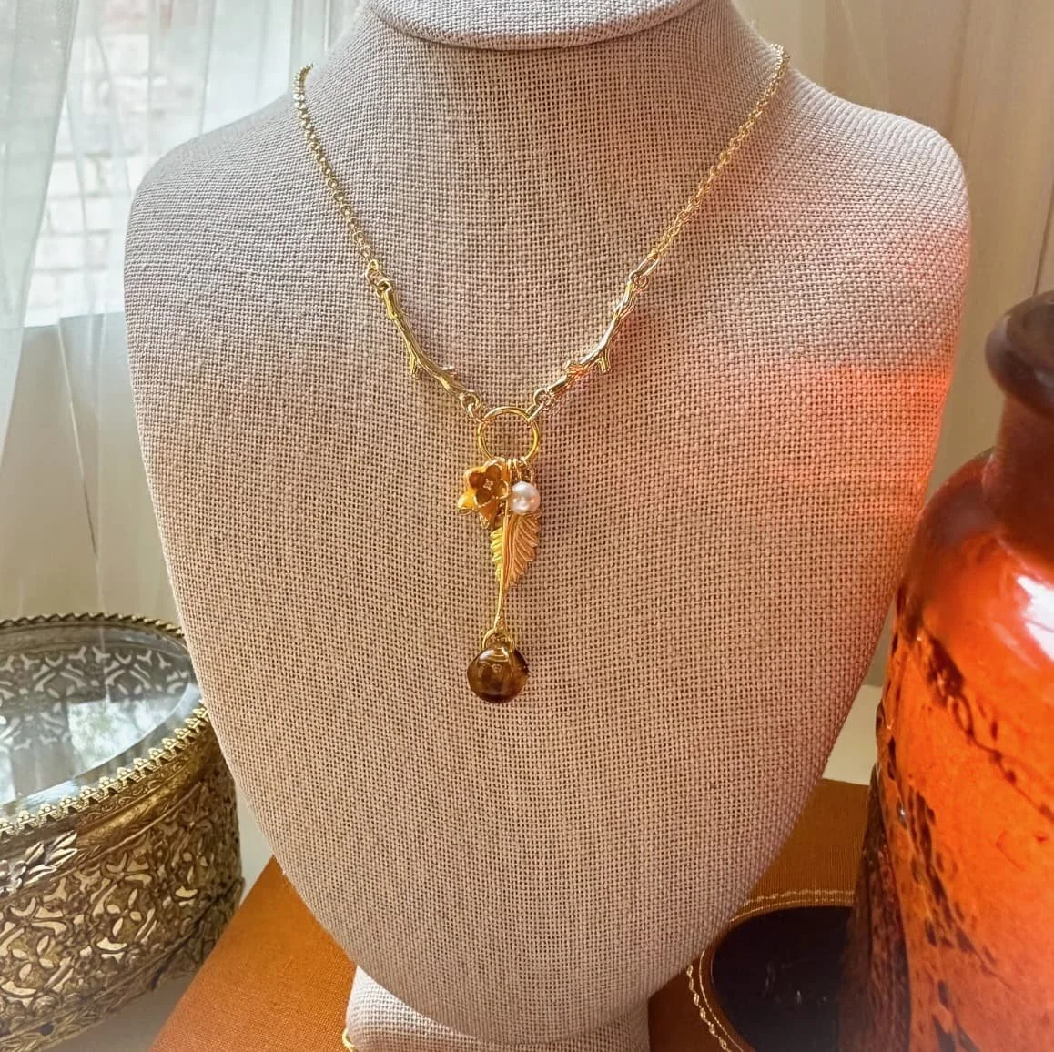 Fal charm necklace with yellow flower charm and amber bead on a mannequin with candle.