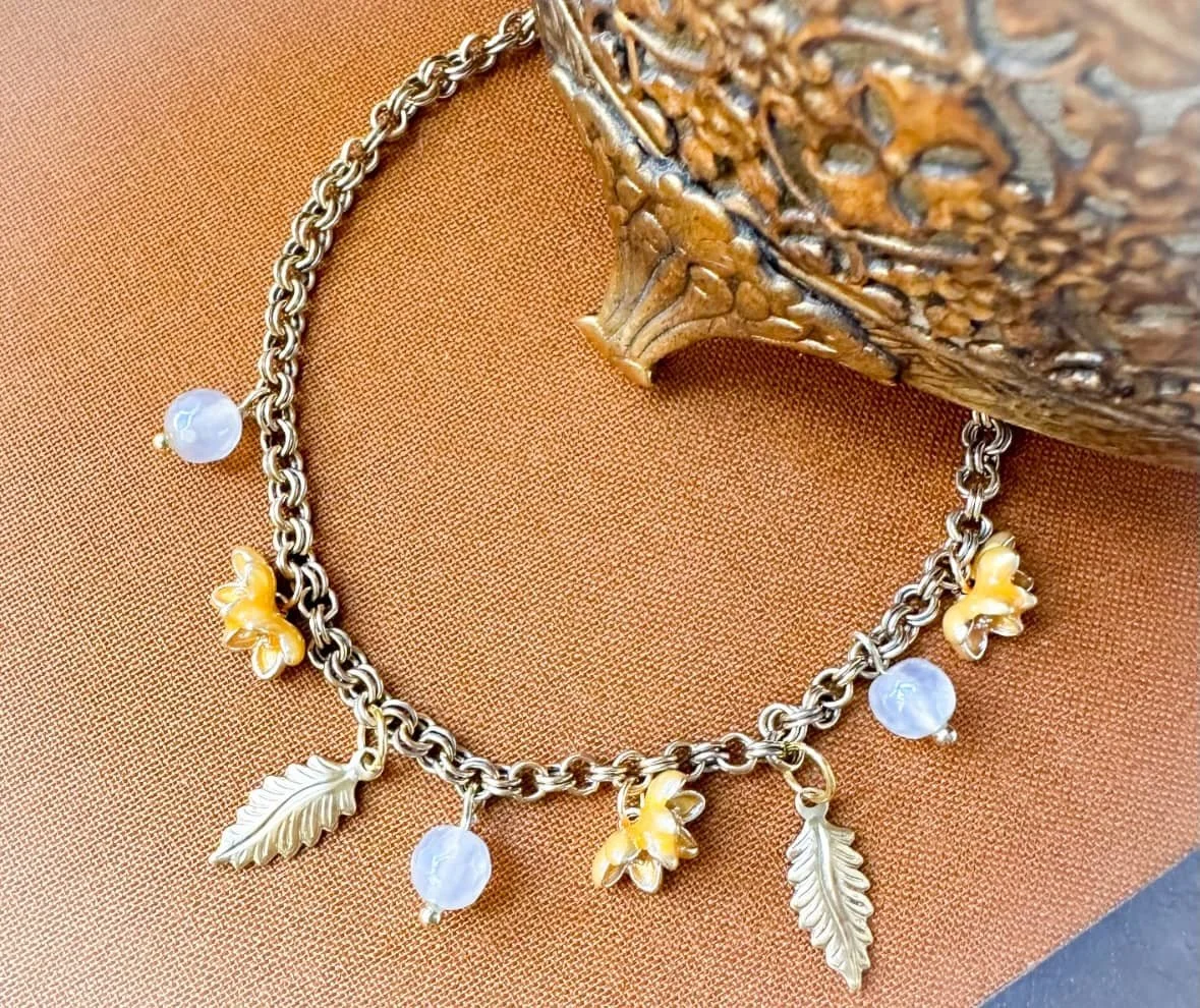 Charm bracelet with yellow flowers, leaves and mystic agate bead with an antique jewelry box.
