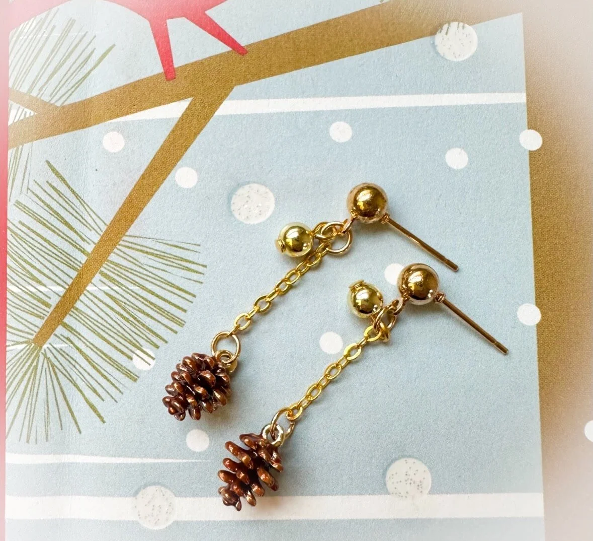 tiny pinecone Christmas earrings on a snowy background.