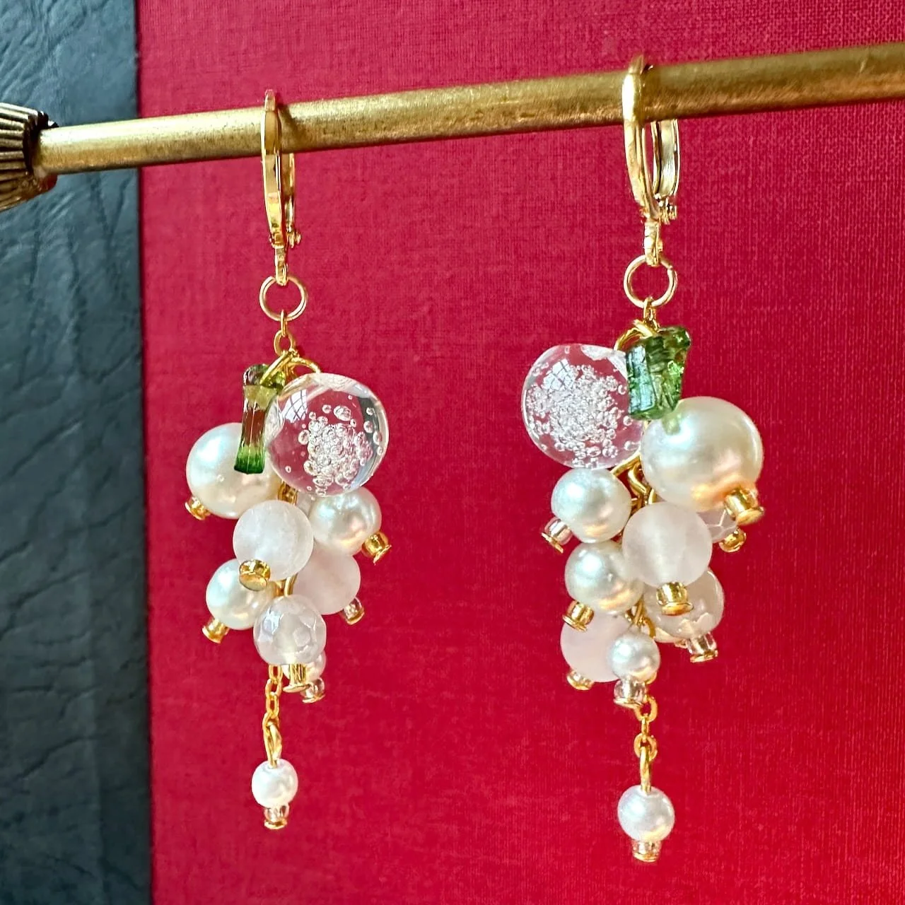 clear snowglobe type beads, pearls dangle earrings on a red background with green leaf.