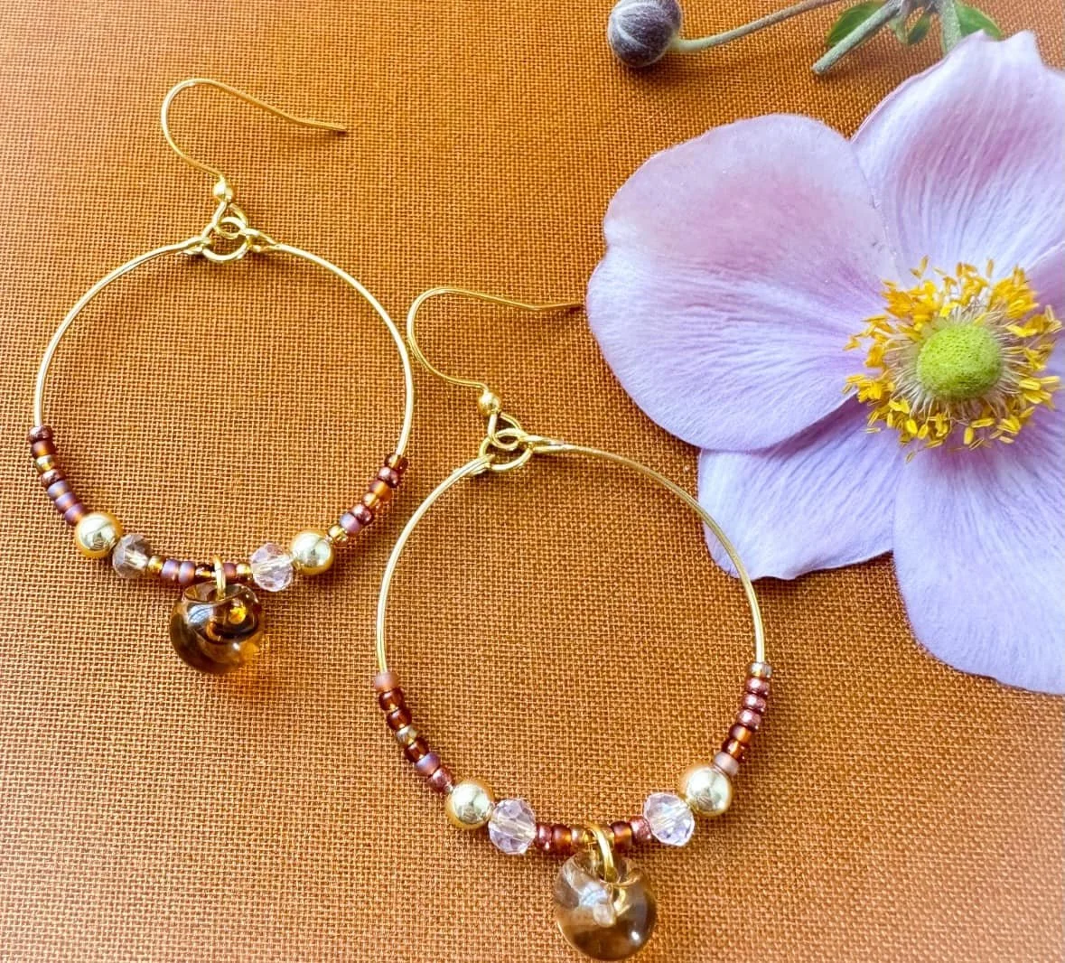 Large hoops on a tan background with amber bead and pink Japanese Anemone flower.