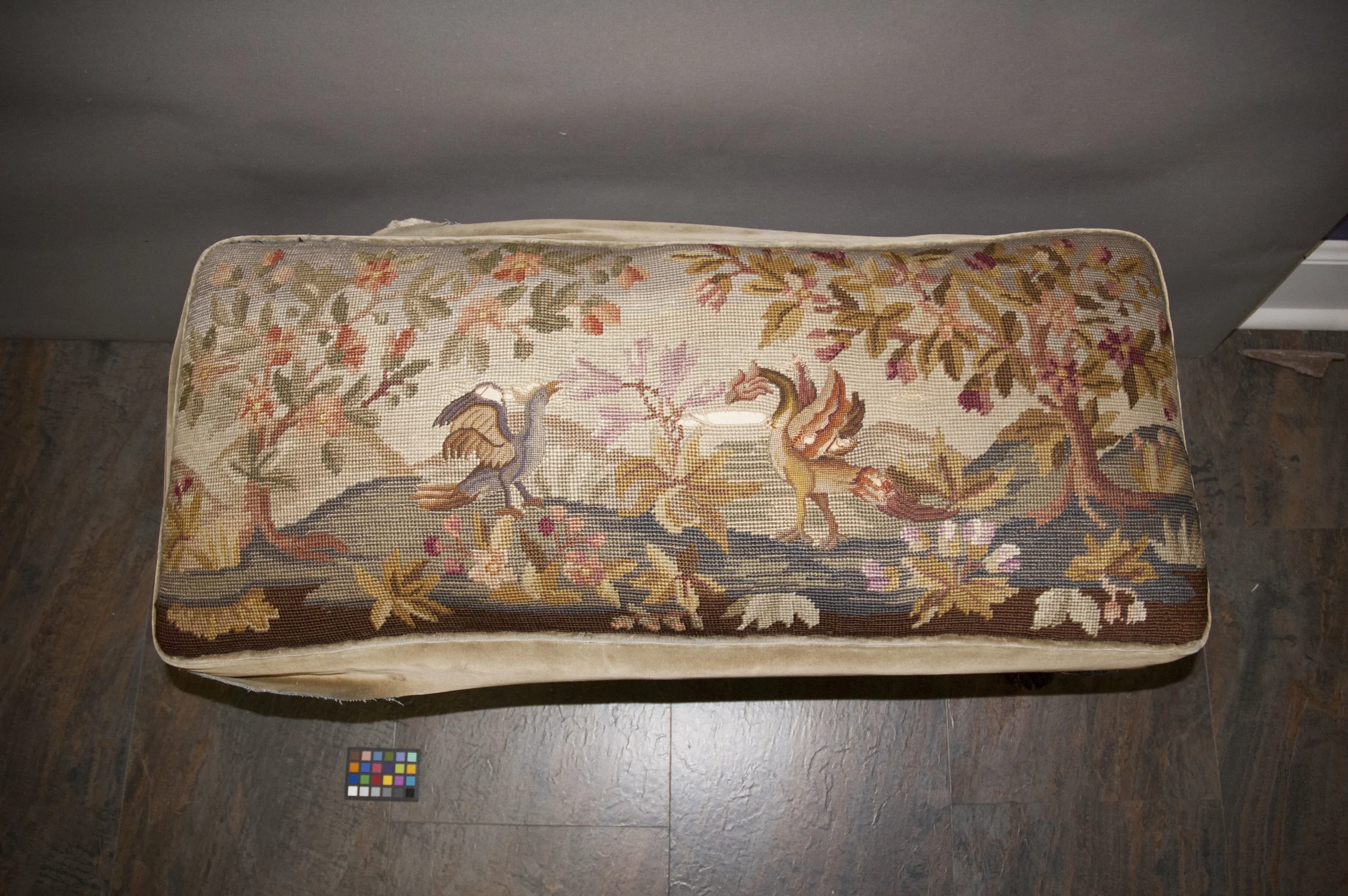 The needlepoint as it arrived, tacked to a small bench