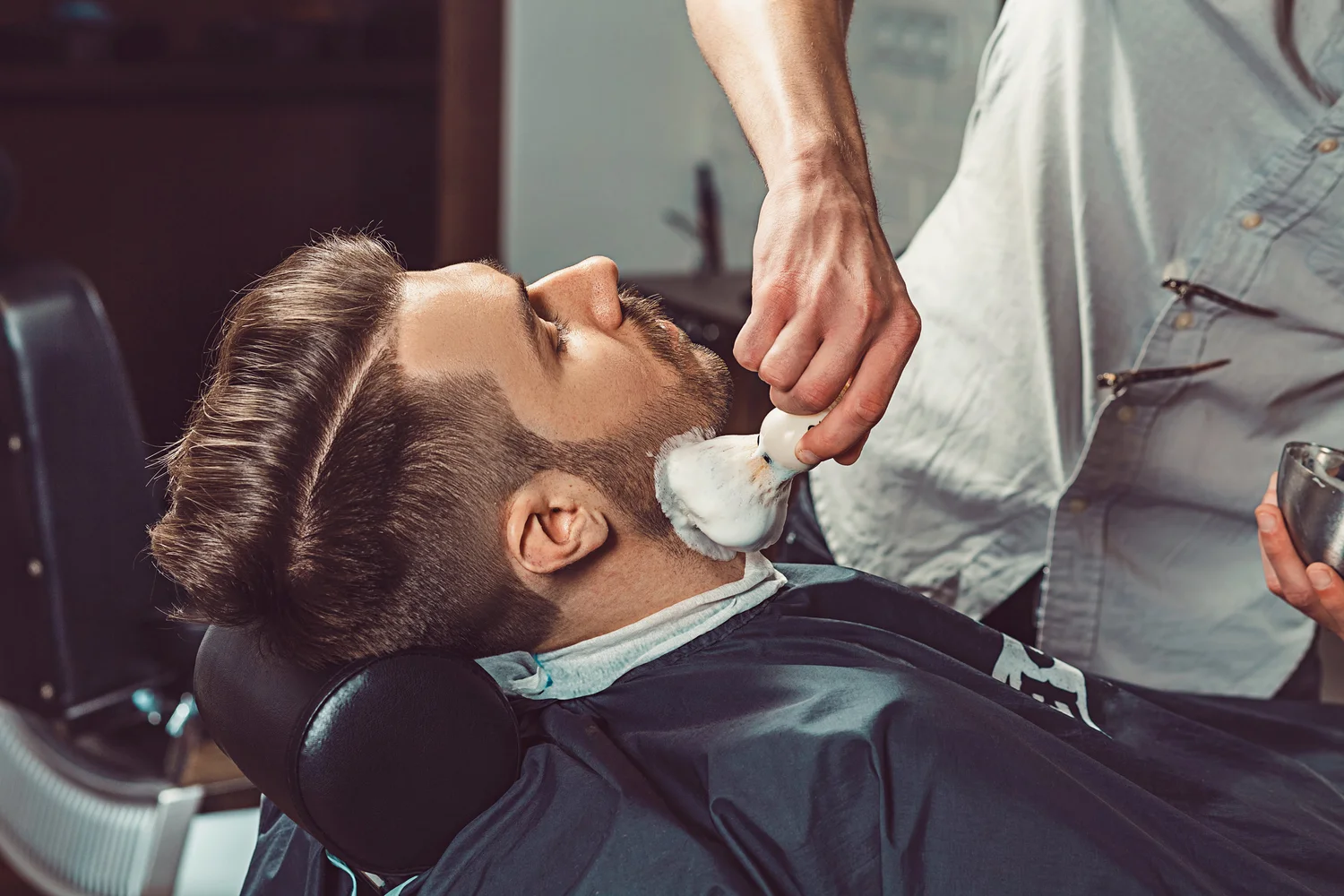 A barber lathers a client's beard before a hot-towel straight-razor shave