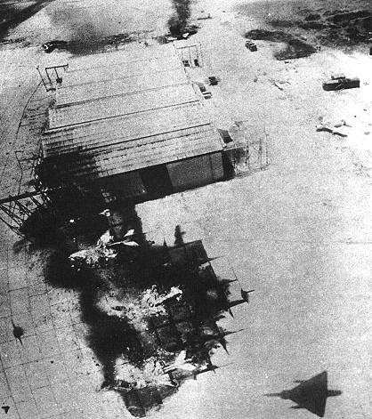 Taken from a low-flying IAF Mirage (whose shadow is visible at the bottom of the picture), three MiG-21s lie destroyed in front of a hangar at Inchas airfield. Photo credit: http://www.oocities.org/capecanaveral/hangar/2848/opera6_2.htm