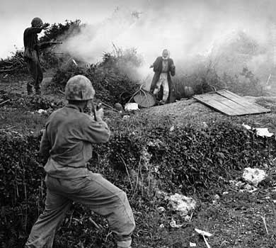Two Marines carefully watch an Okinawan civilian surrendering.