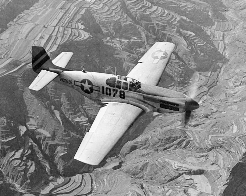 A Merlin-engined P-51B Mustang in flight. This aircraft uses the earlier framed canopy, which was replaced by the Macolm hood, a rounded Plexiglas canopy that omitted metal frames and allowed for increased visibility. Source: Wikipedia.