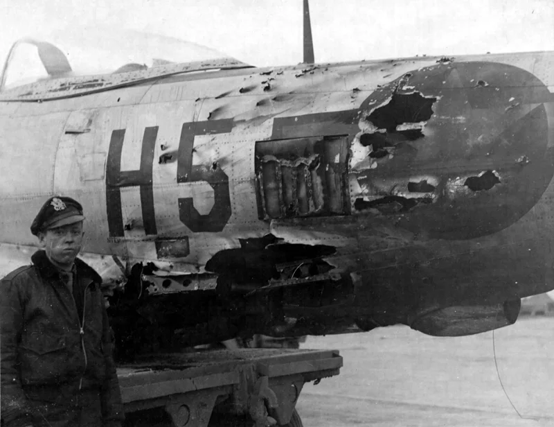 A P-47 pilot displays a rather sober face after examining his P-47, which has sustained a direct hit from a flak round of unknown caliber. Photo source: Pinterest.