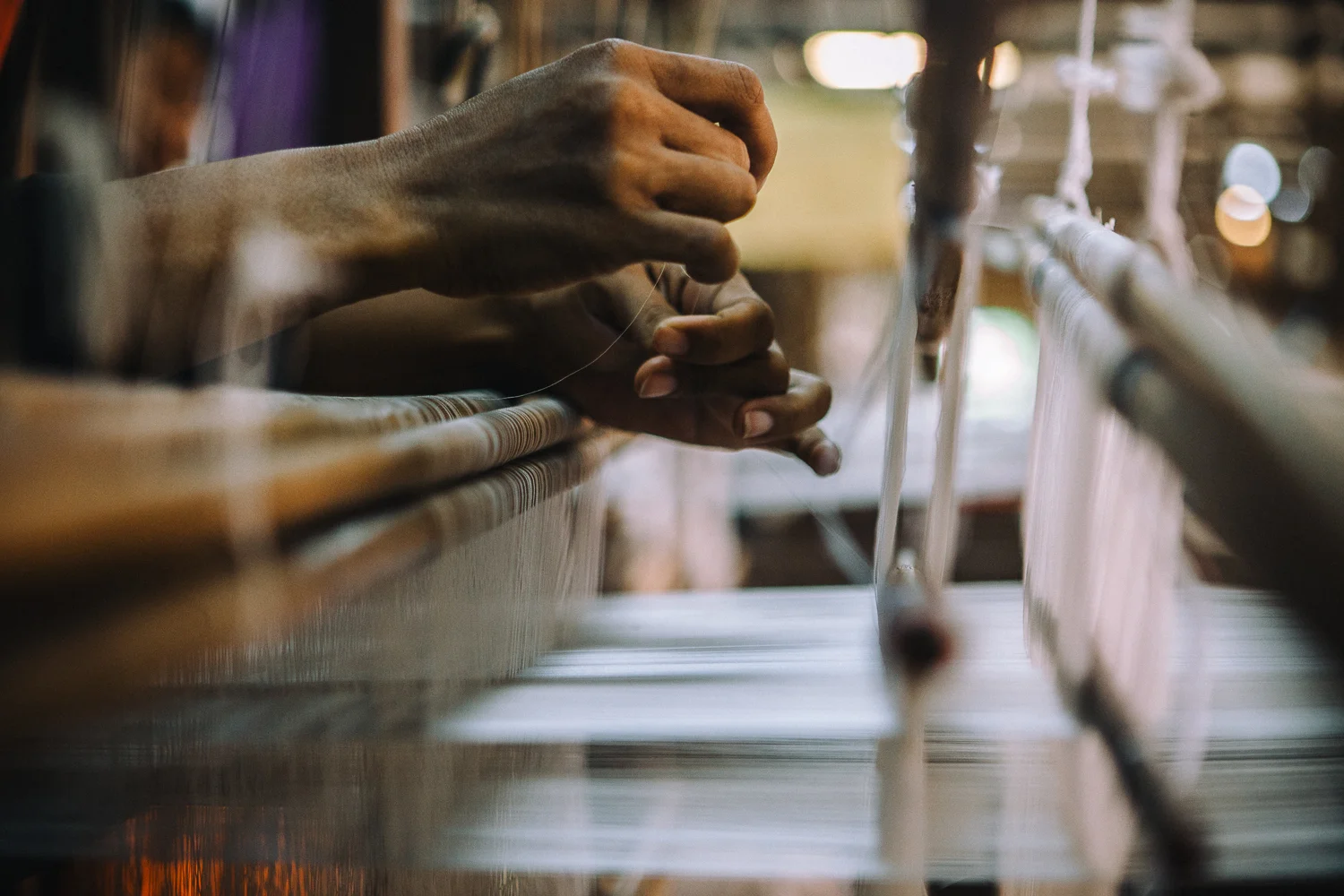 An artisan threads silk into a manual weaving machine