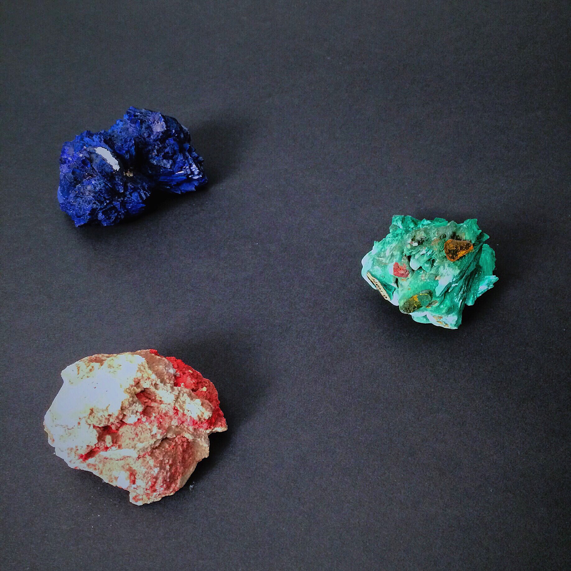 These minerals are idiochromatic. Their color is constant and predictable. Moving clockwise from the top left: azurite, malachite, and cinnabar. Minerals are from the Bruce Museum's collection. Photo by Haley Royer.