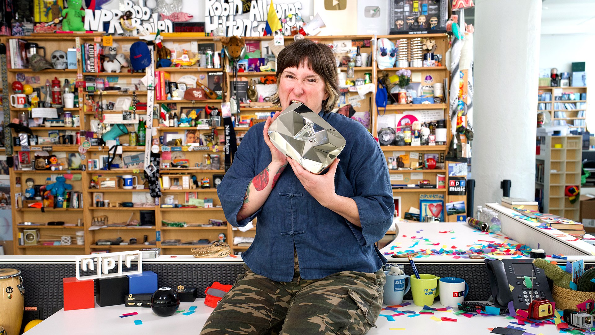Kara Frame sitting on the Tiny Desk biting the YouTube diamond award for 10 million subscribers.