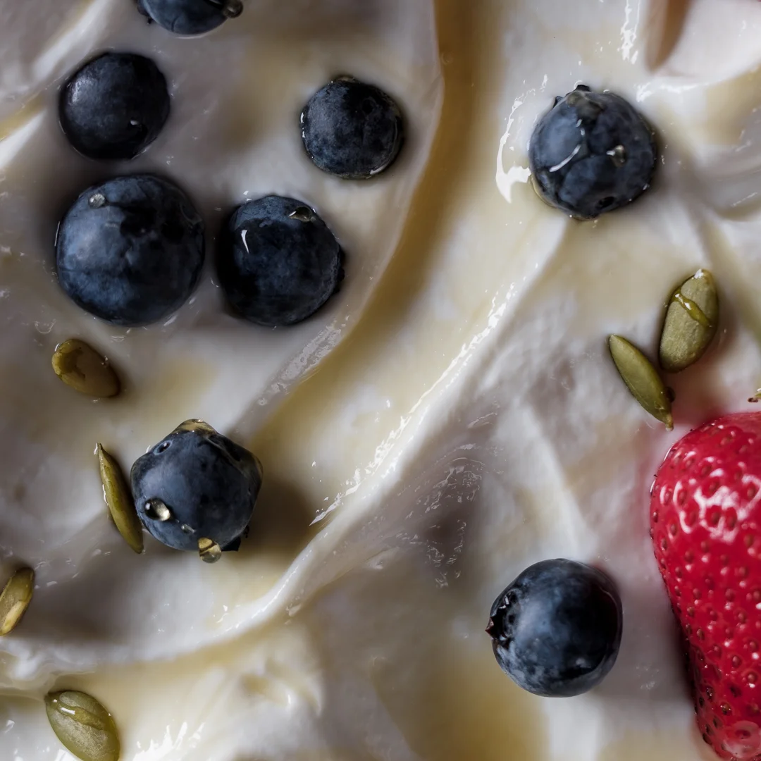 Close up of greek yogurt and fresh berries Close up detail shot of a field of white greek yogurt drizzled with honey and topped with fresh blueberries and a strawberry.