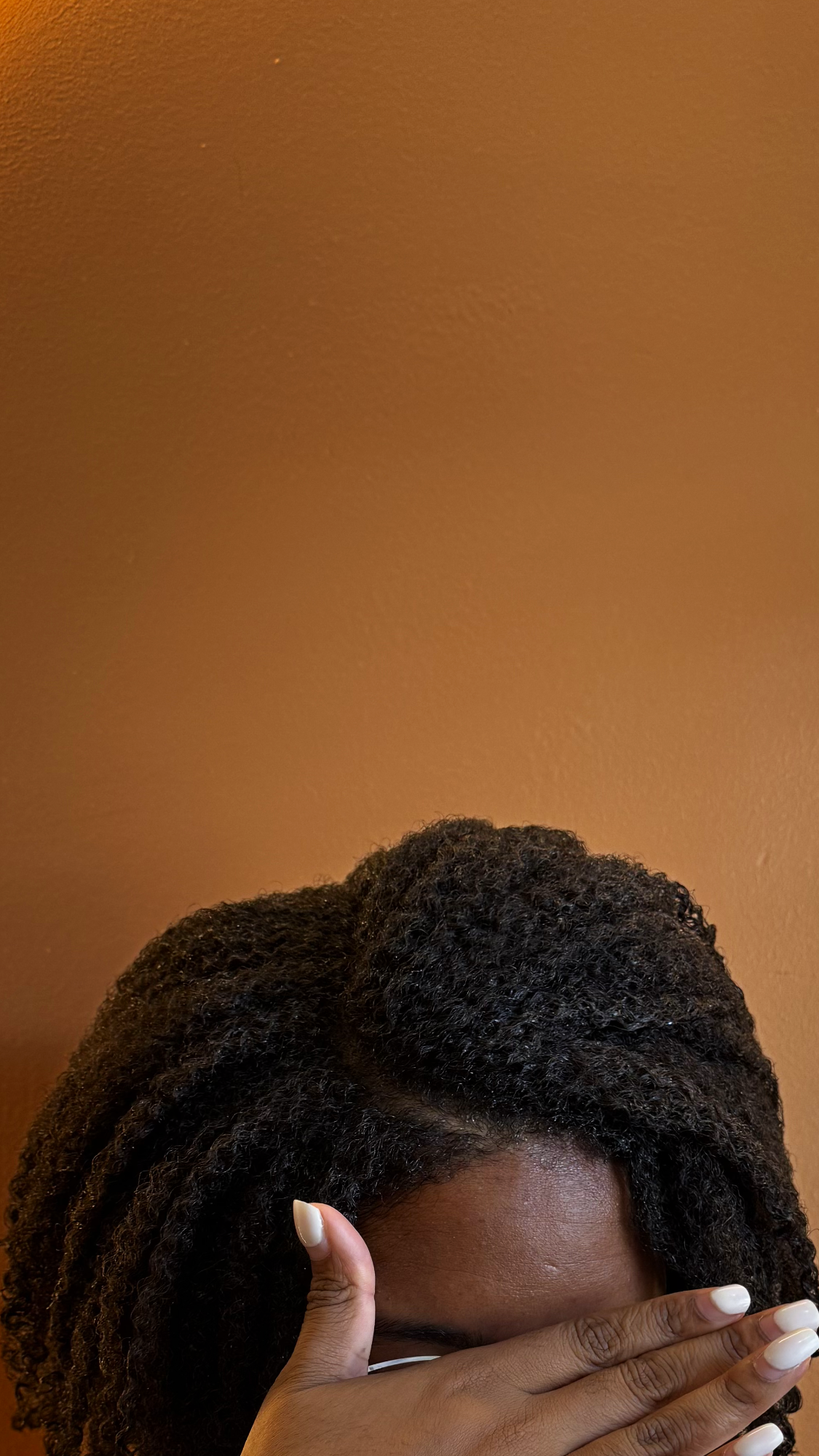 A photo of 4C textured hair in front of an orange wall