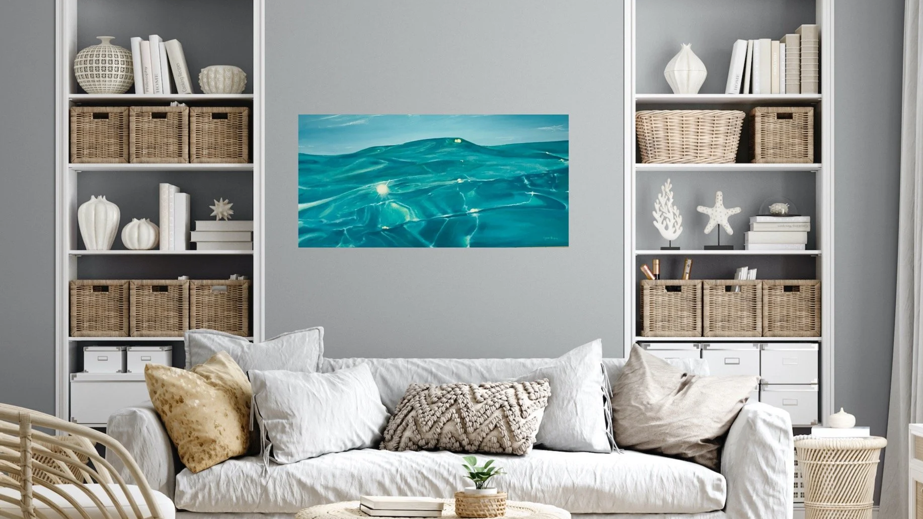 Living room with white sofa, beige pillows, and two white bookshelves filled with wicker baskets and decorative objects, and a framed picture of ocean waves on the wall.