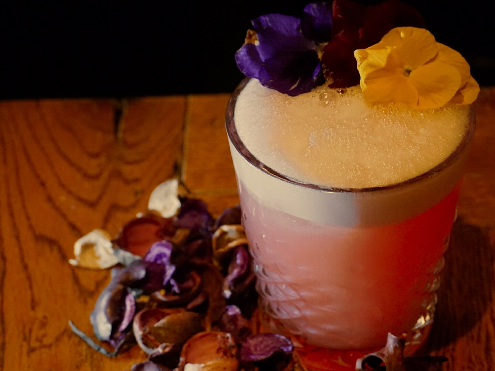  A forthy pink cocktail garnished with a purple flower and a yellow flower. 