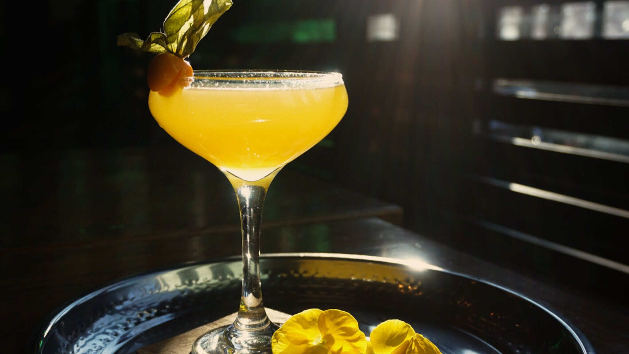  A vibrant yellow cocktail on a tray with a beam of sunlight giving an almost glowing effect. 