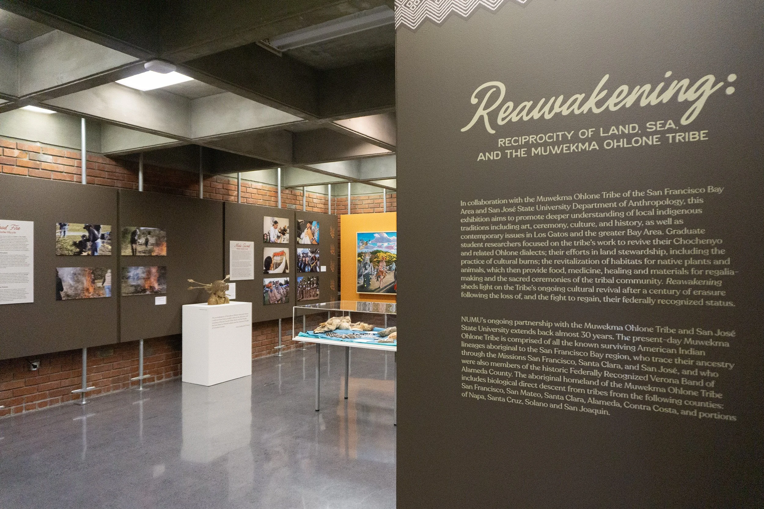 The gallery, partially obcured by a title wall which reads, "Reawakening," featuring photos, sculptures, and more