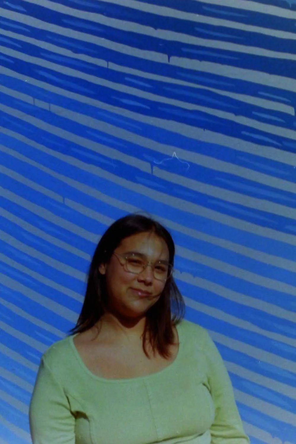 A blue toned photo of a woman in a yellow shirt and glasses, posing