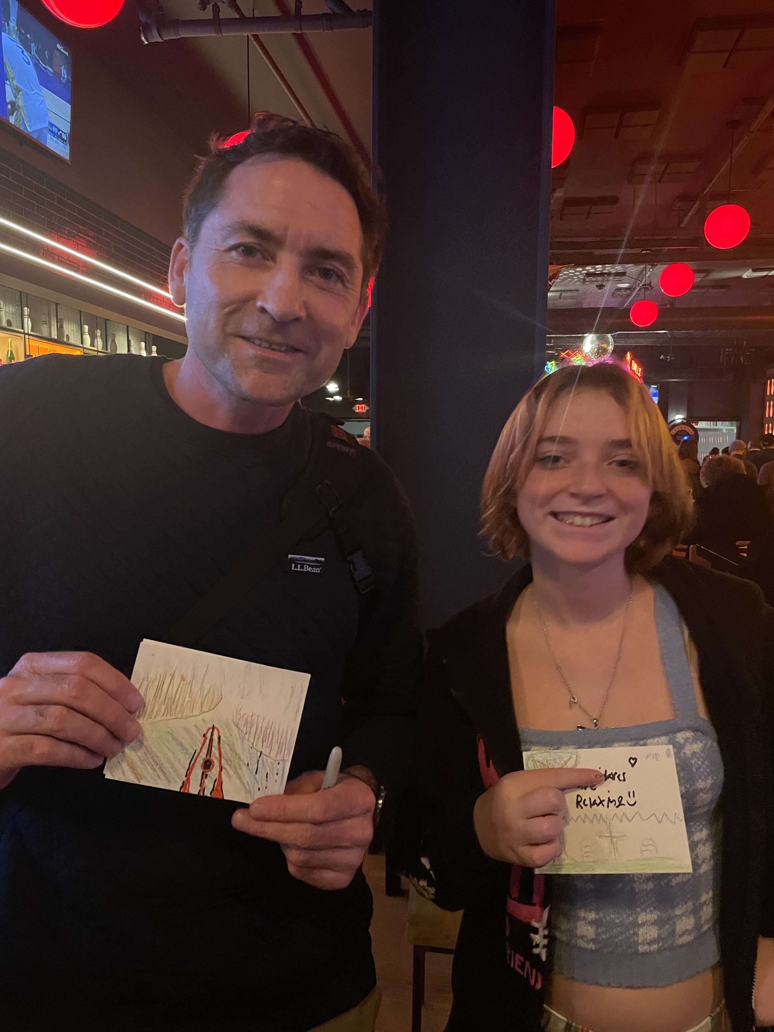 A father and teenager holding up postcards they drew
