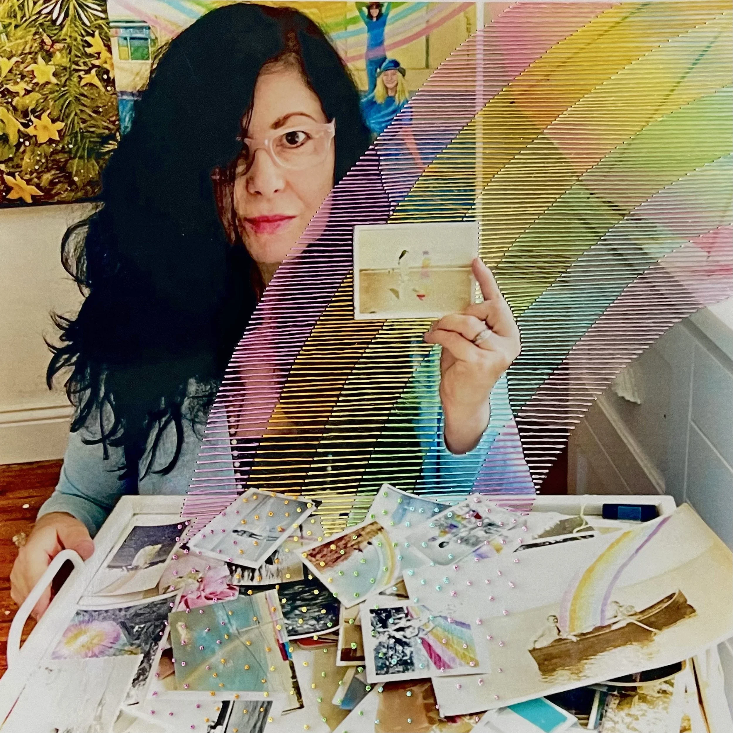 Marie sits at a table covered in postcards, she holds one up. The entire image has a rainbow embroidered on it.