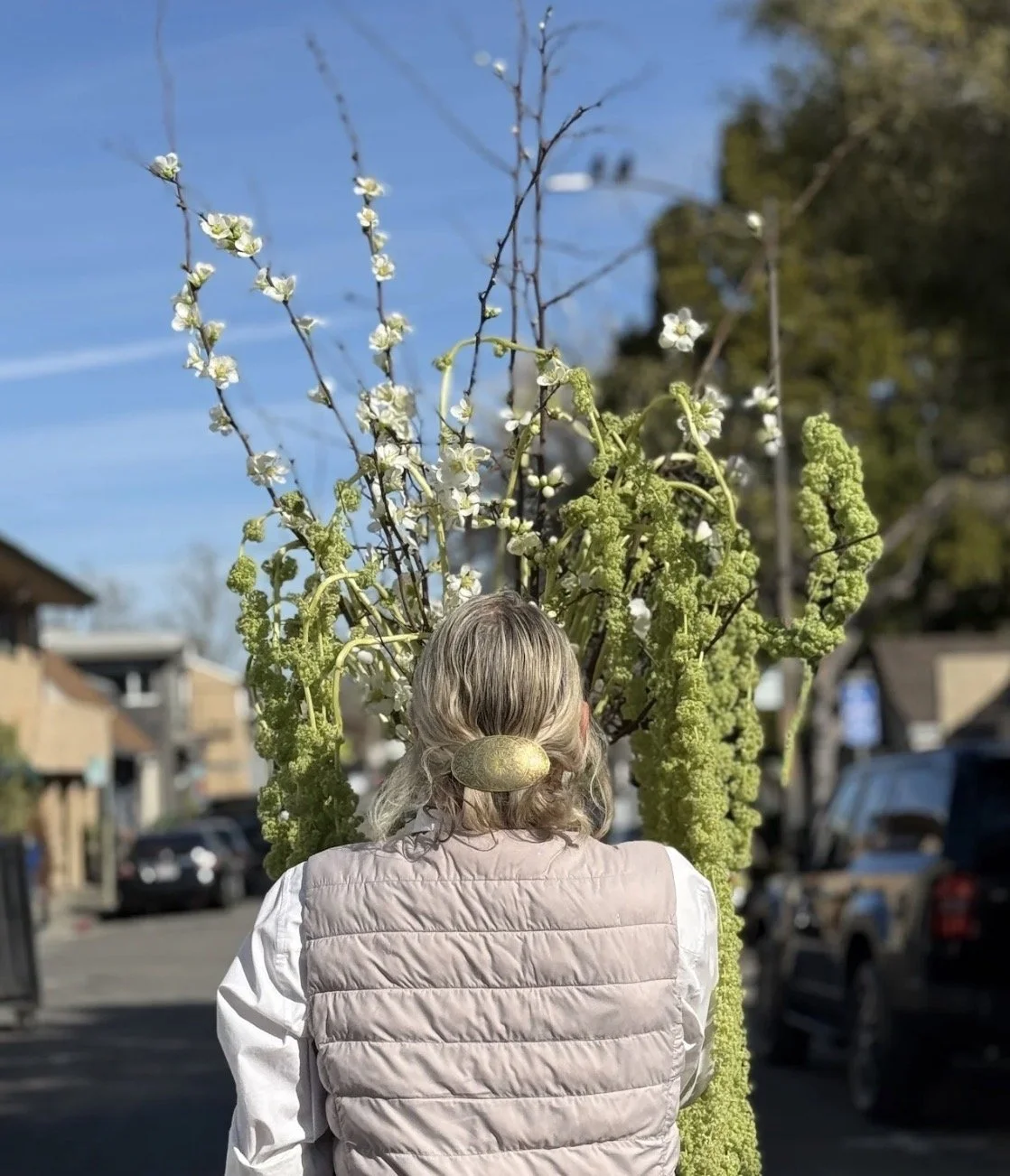 Catherine, her back to the camera, walks down a street holding a bouquet that towers over her head.
